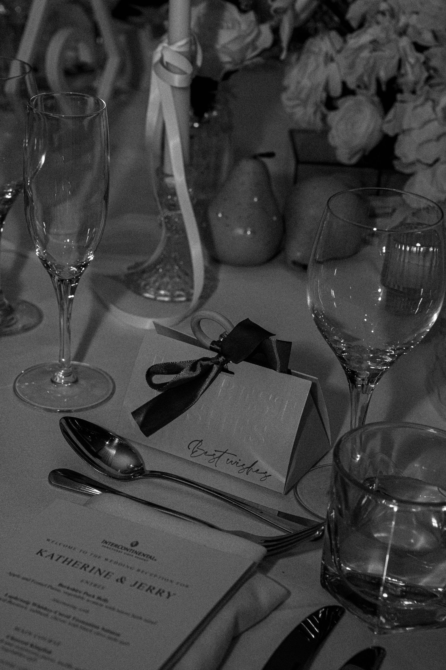 Black and white photograph of elegant place settings with name cards and wine glasses at a formal dinner table.