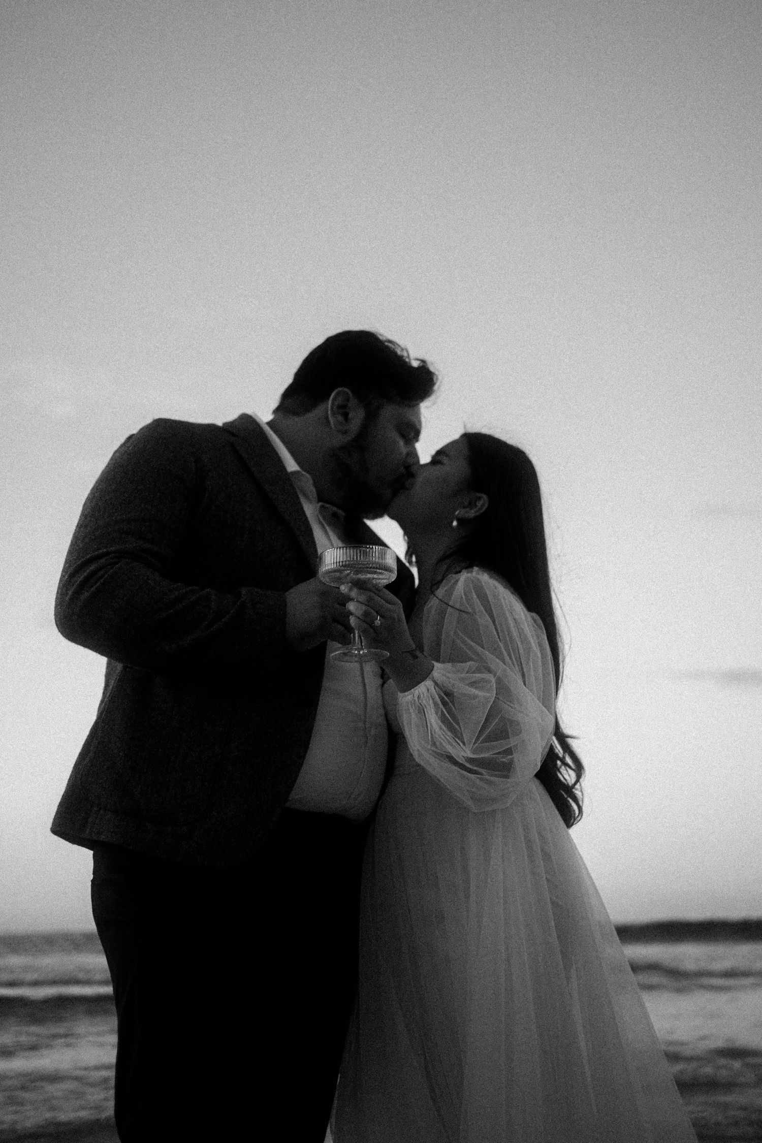 A romantic black and white photo sequence shows a couple in wedding attire sharing intimate kisses on a beach at sunset.