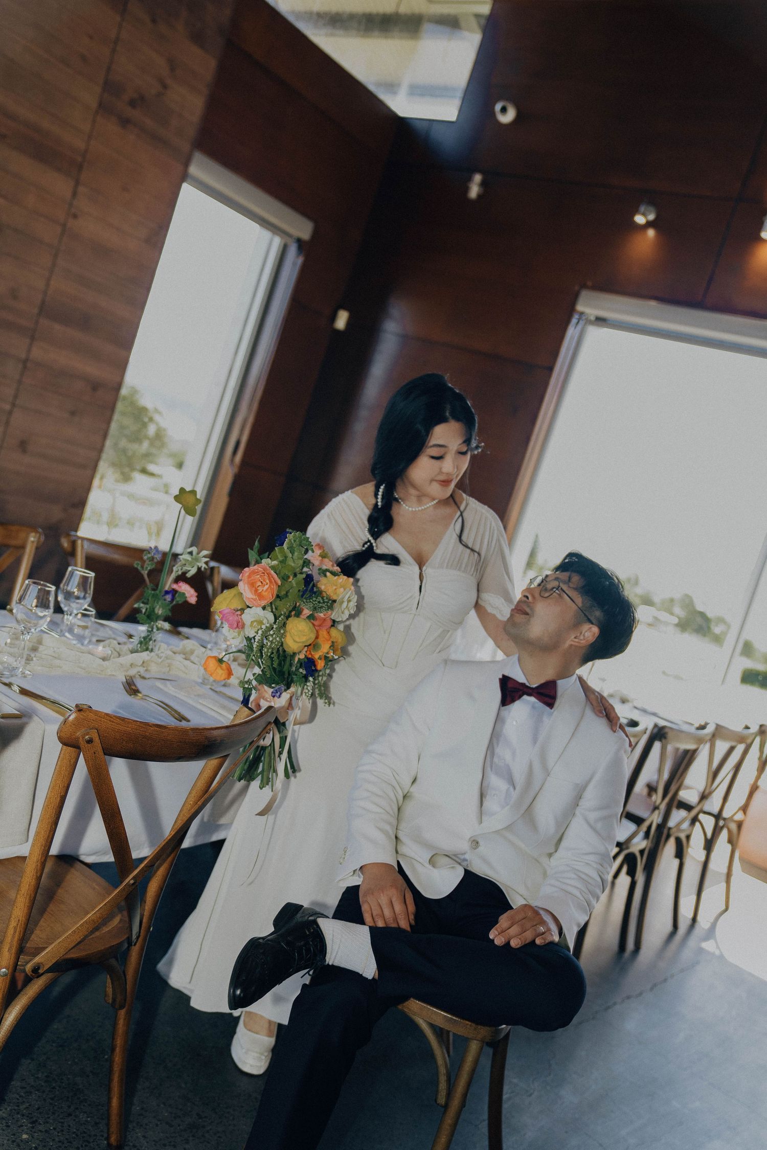 A couple in formal attire shares an intimate moment at a rustic restaurant with wooden decor and floral arrangements.