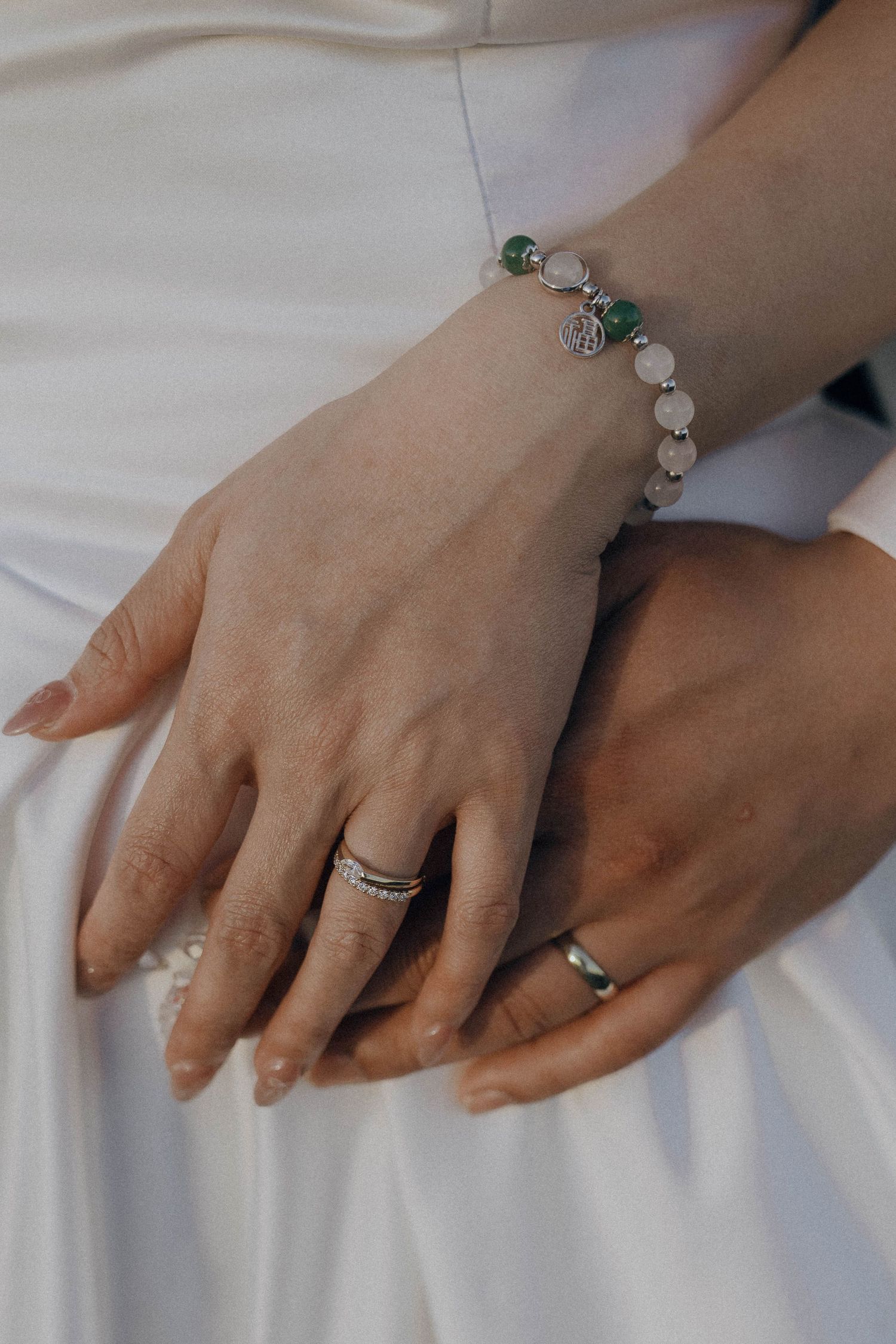 Close-up sequence of hands wearing delicate rings and bracelets against white fabric background.