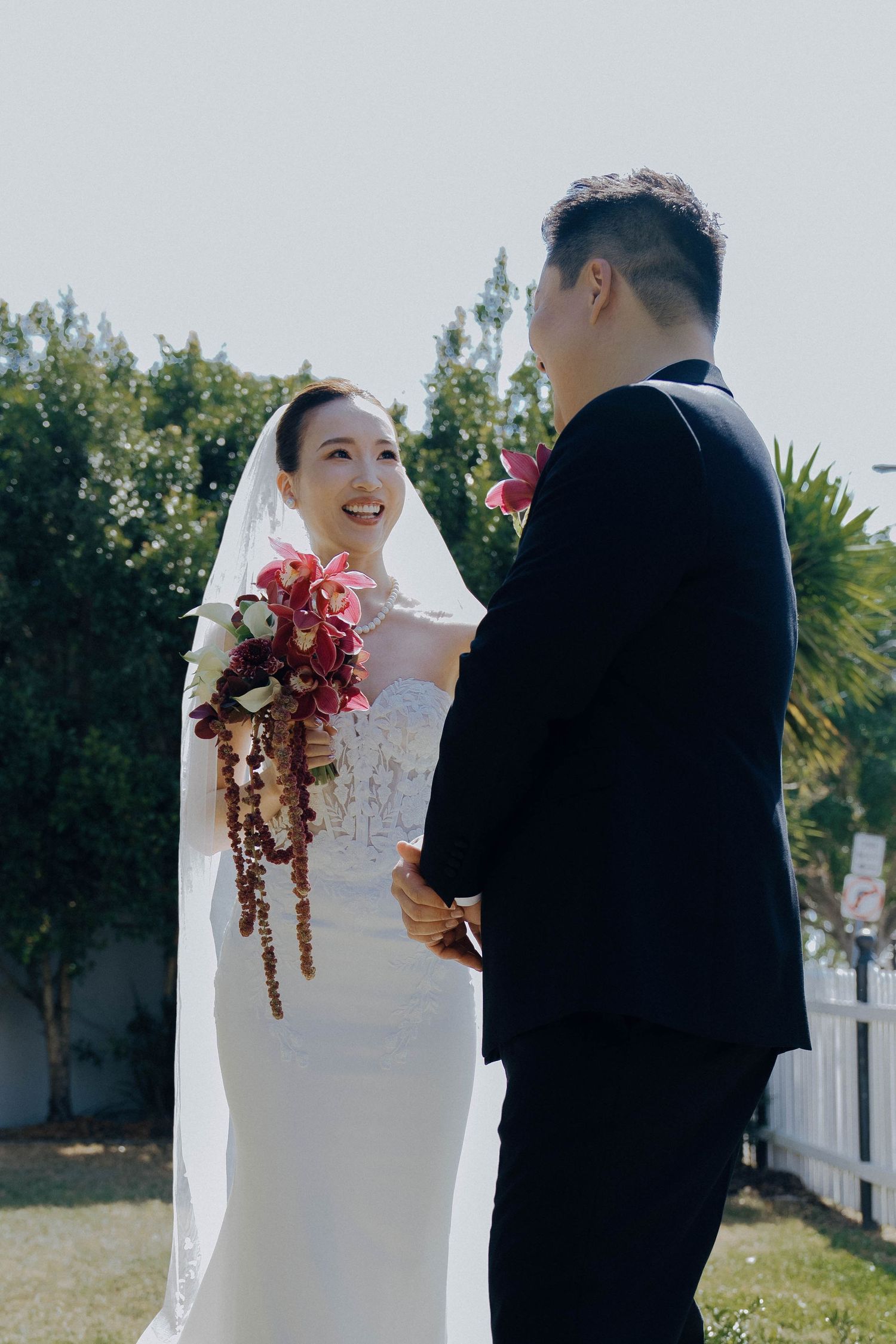 Bride and groom share intimate moments during their outdoor wedding ceremony with white picket fences and greenery in background.