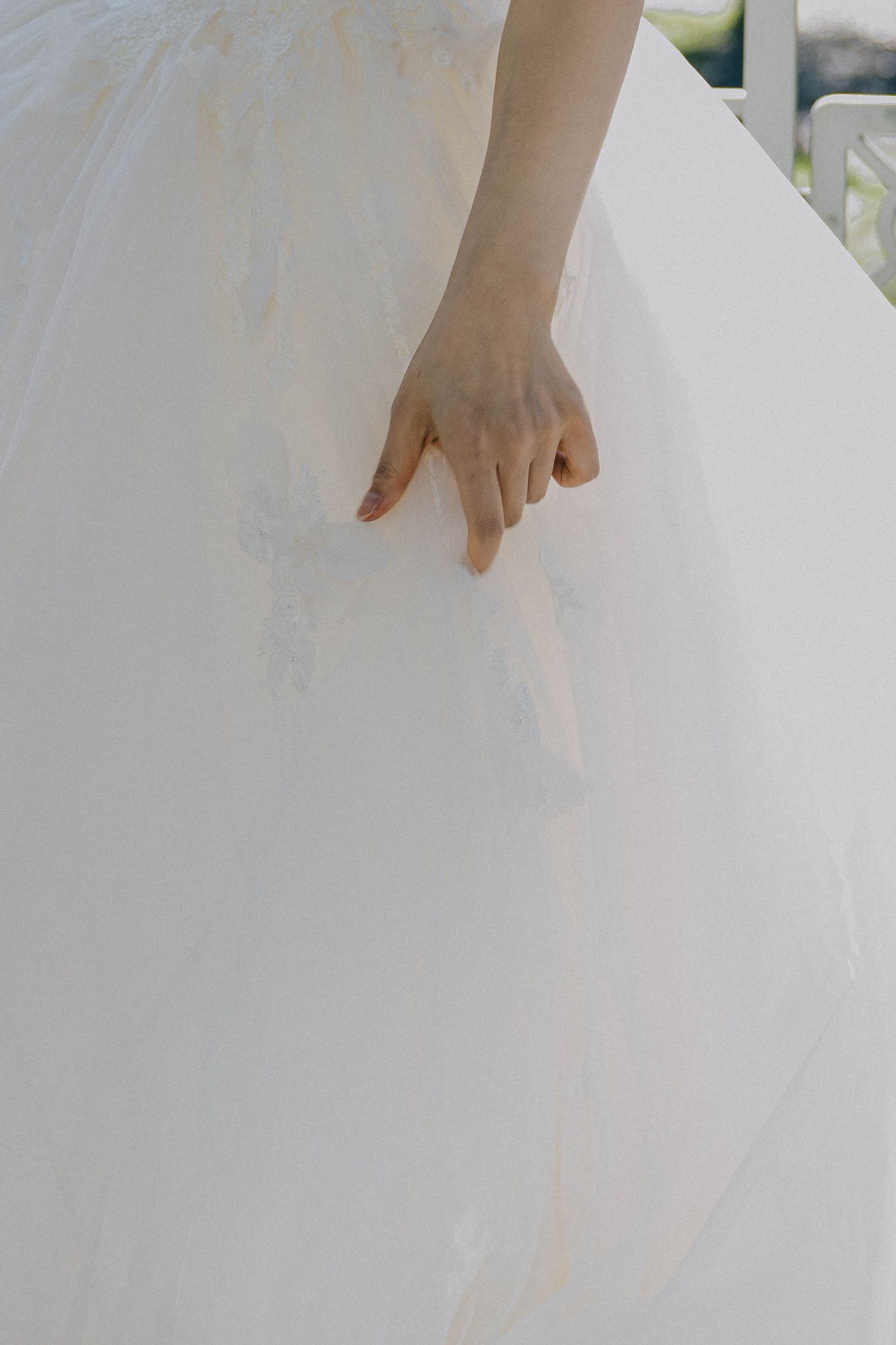 A delicate hand gently holds the fabric of a flowing white wedding dress.