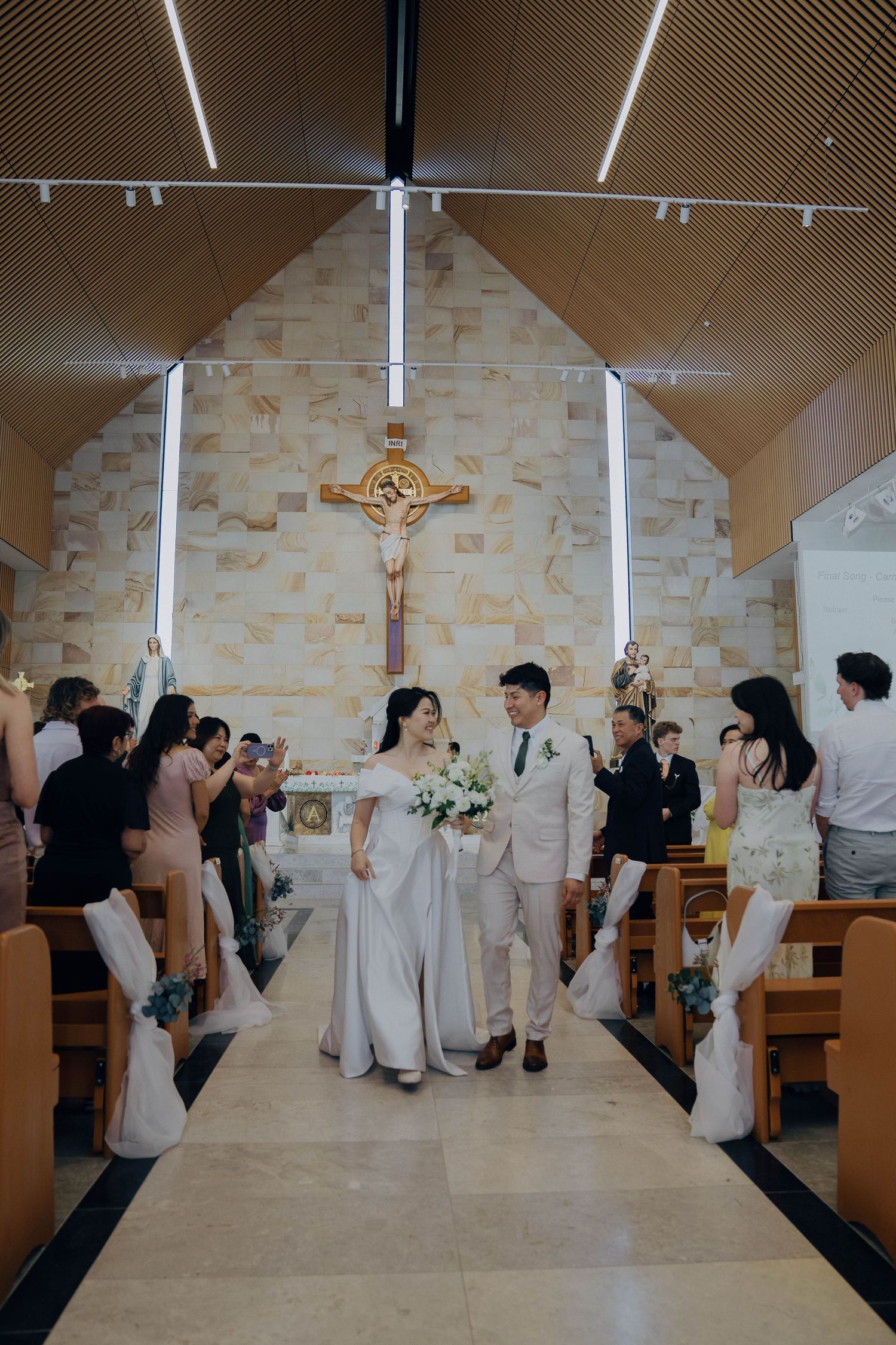 Wedding party performs synchronized dance moves in a modern church sanctuary with stone walls and wooden pews.