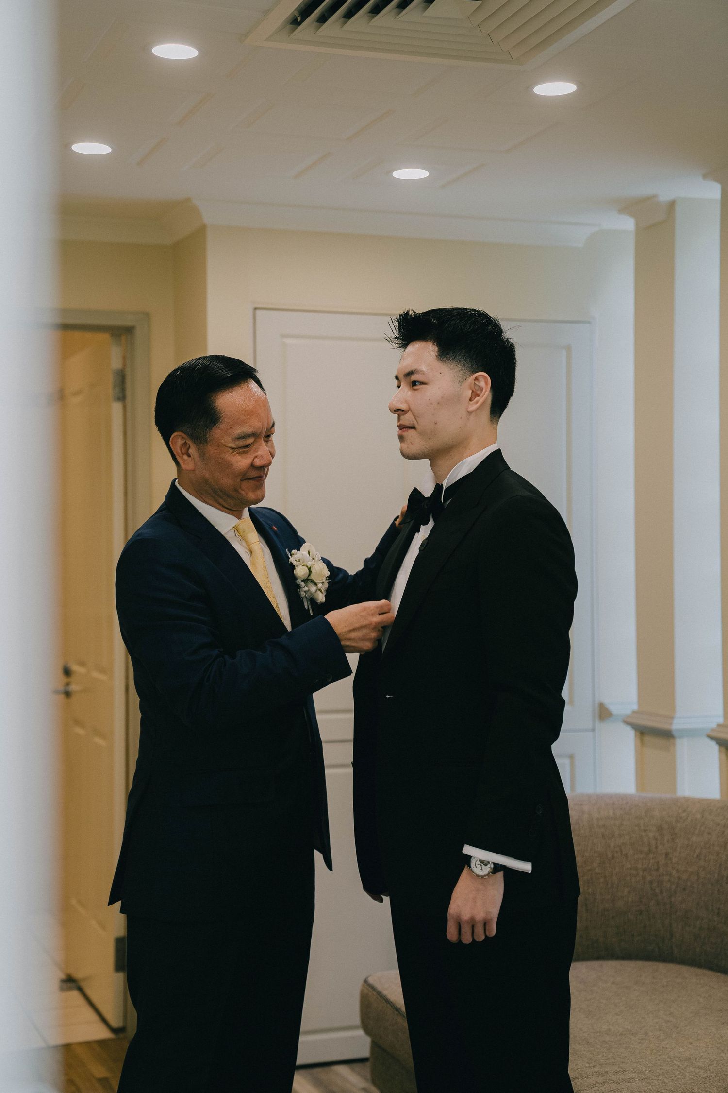 Two people in dark suits having an animated conversation in a brightly lit office hallway.