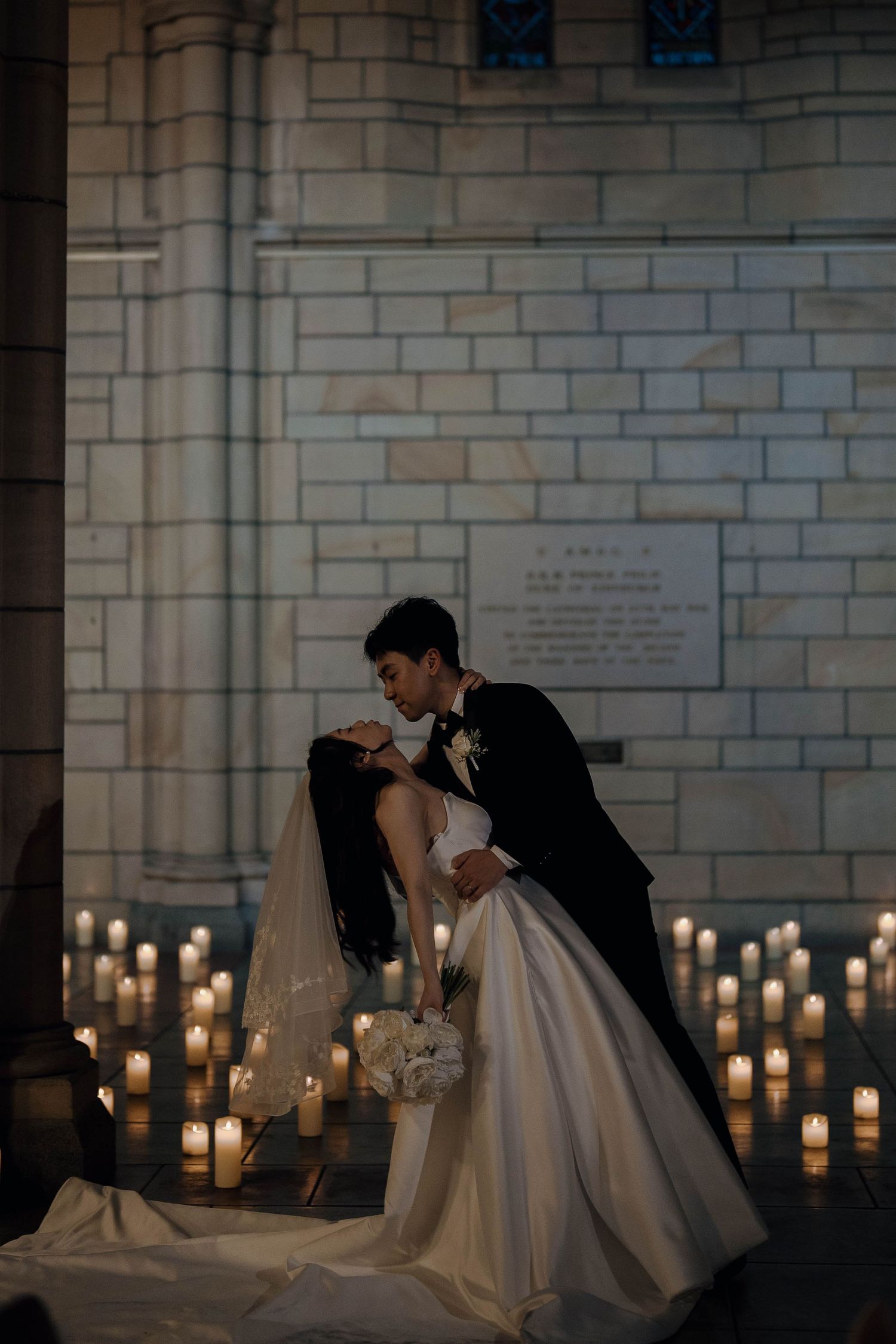 A romantic wedding scene with a couple in formal attire sharing an intimate moment surrounded by glowing candlelight.