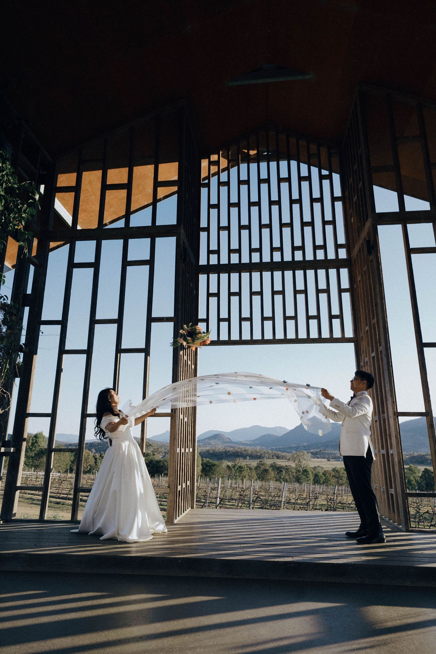 A couple dances together in a modern pavilion with large windows overlooking scenic mountain views at sunset.