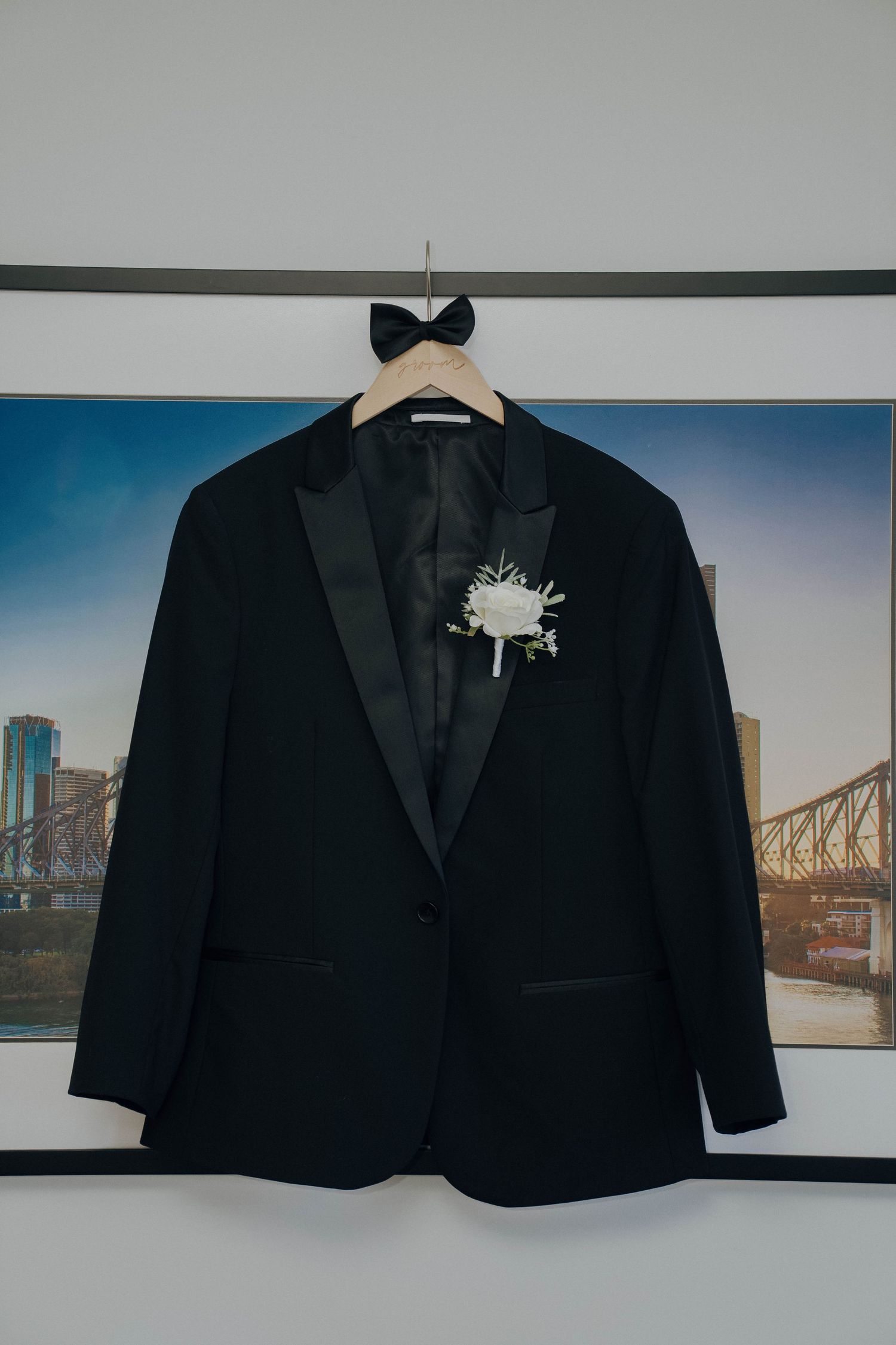 Black formal blazer jacket displayed against wall with bridge artwork in background.