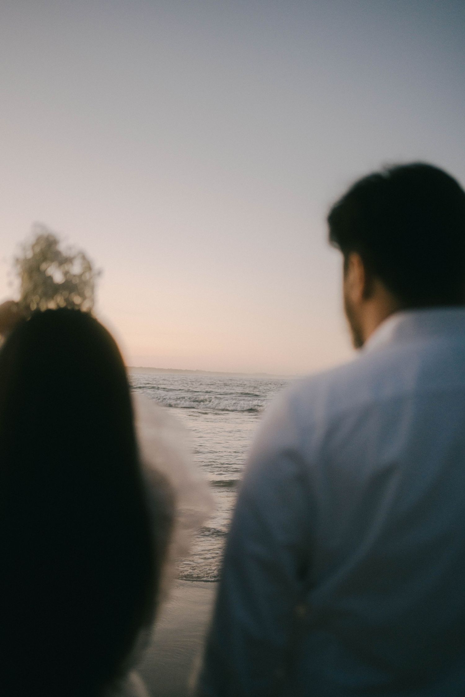 A couple sits silently watching the sunset over the ocean horizon in a series of dreamy, romantic silhouettes.