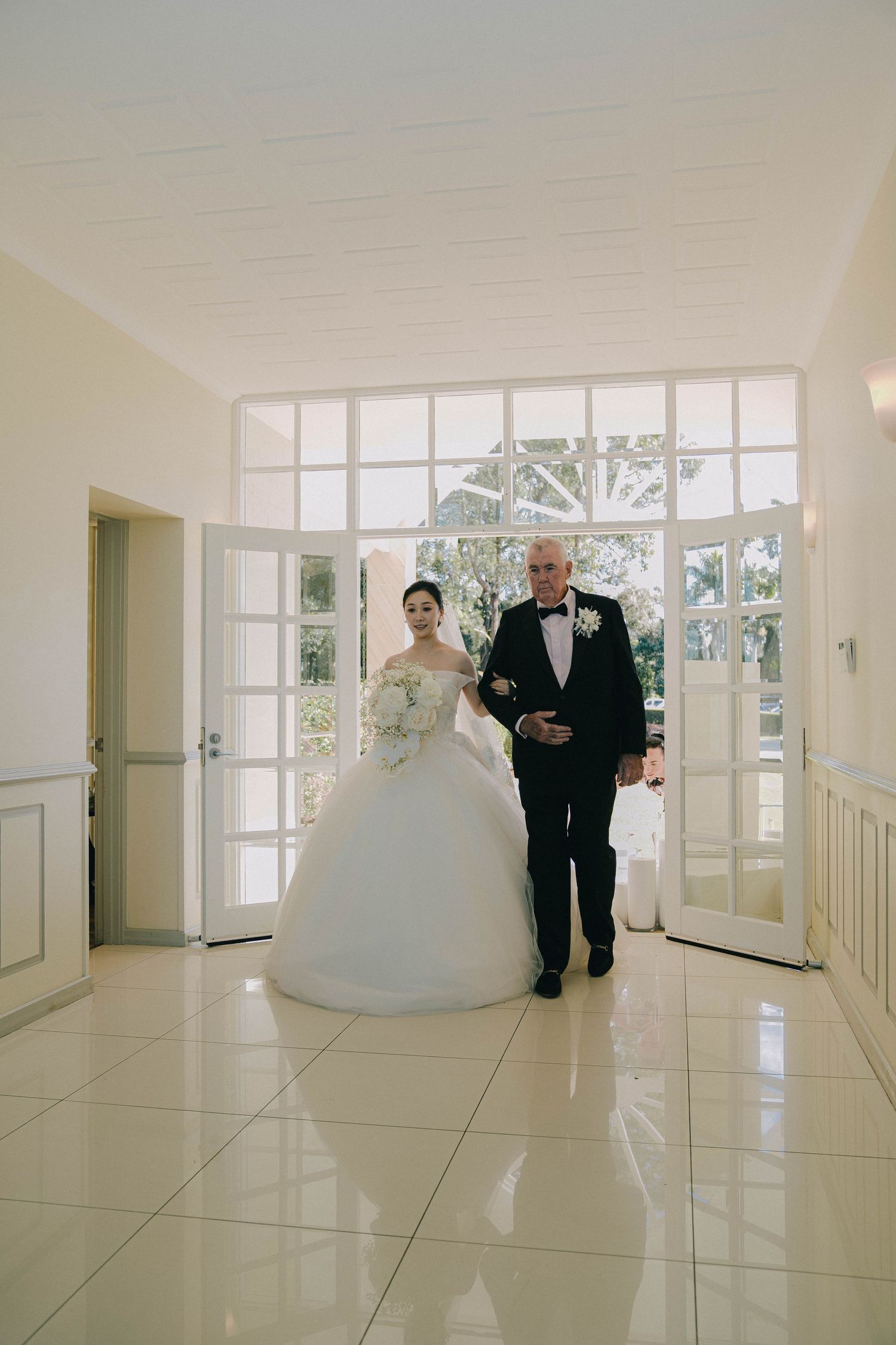 A series of photos showing a wedding couple walking through a bright, modern hallway with white tiled floors and large windows.