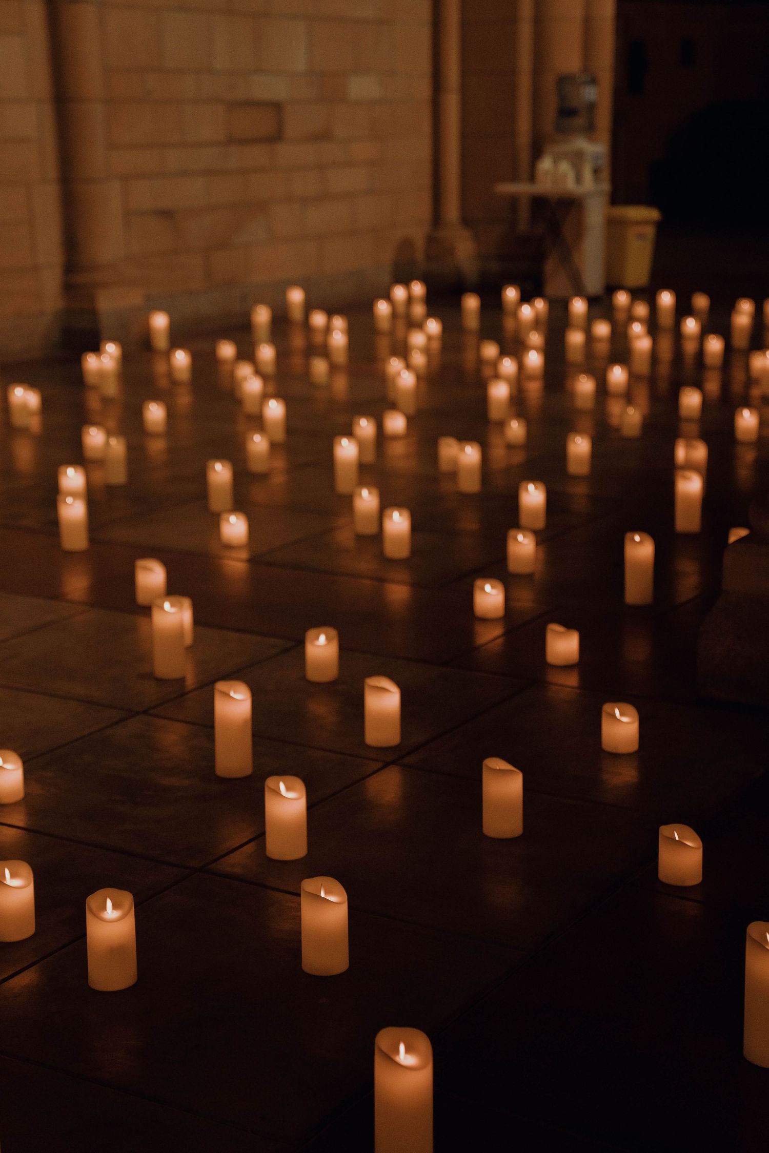 Multiple glowing white candles create a warm, atmospheric display on a dark wooden surface in low light conditions.