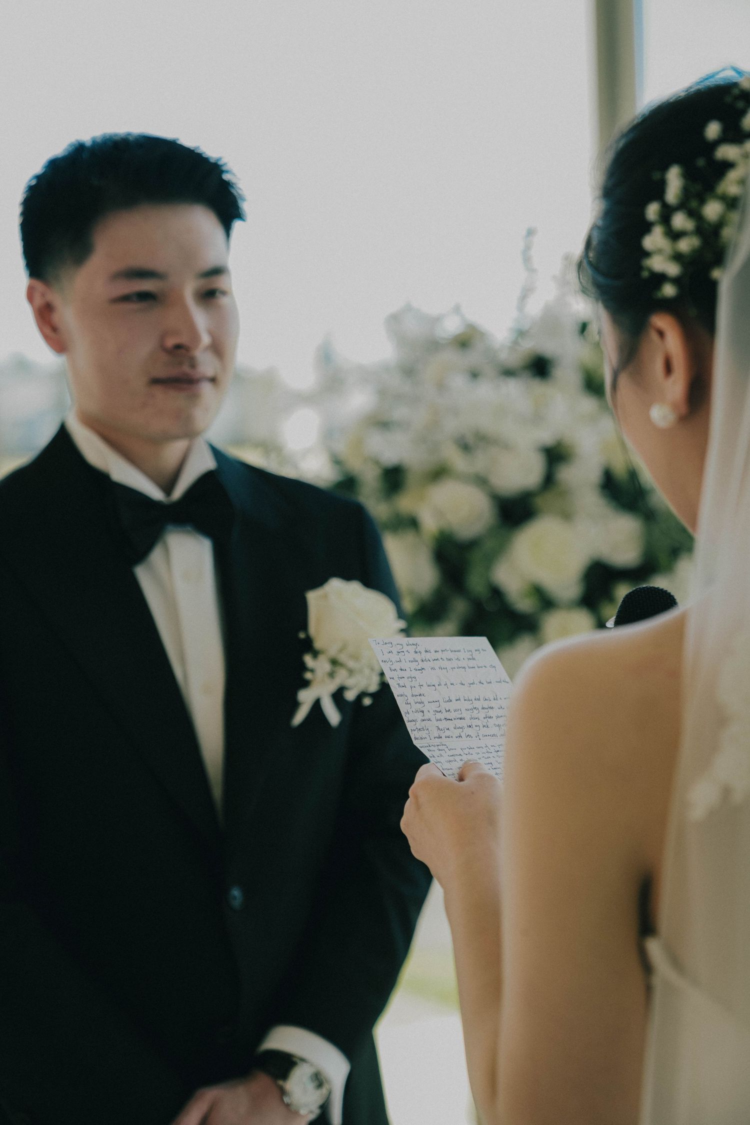 A tender moment between newlyweds during their wedding ceremony with white floral decorations in the background.