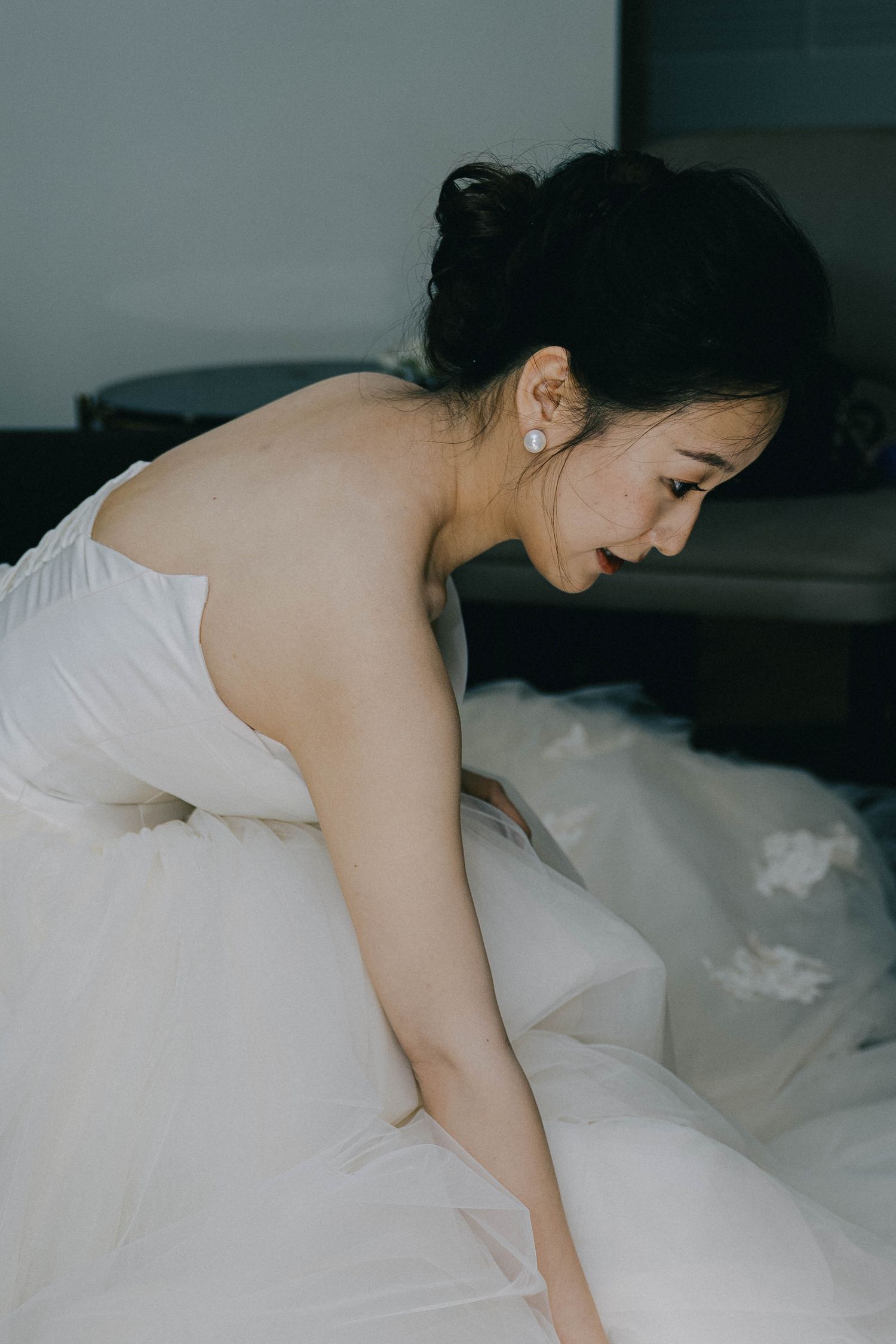 Person in white sleepwear lying on bed with white bedding in dimly lit room.