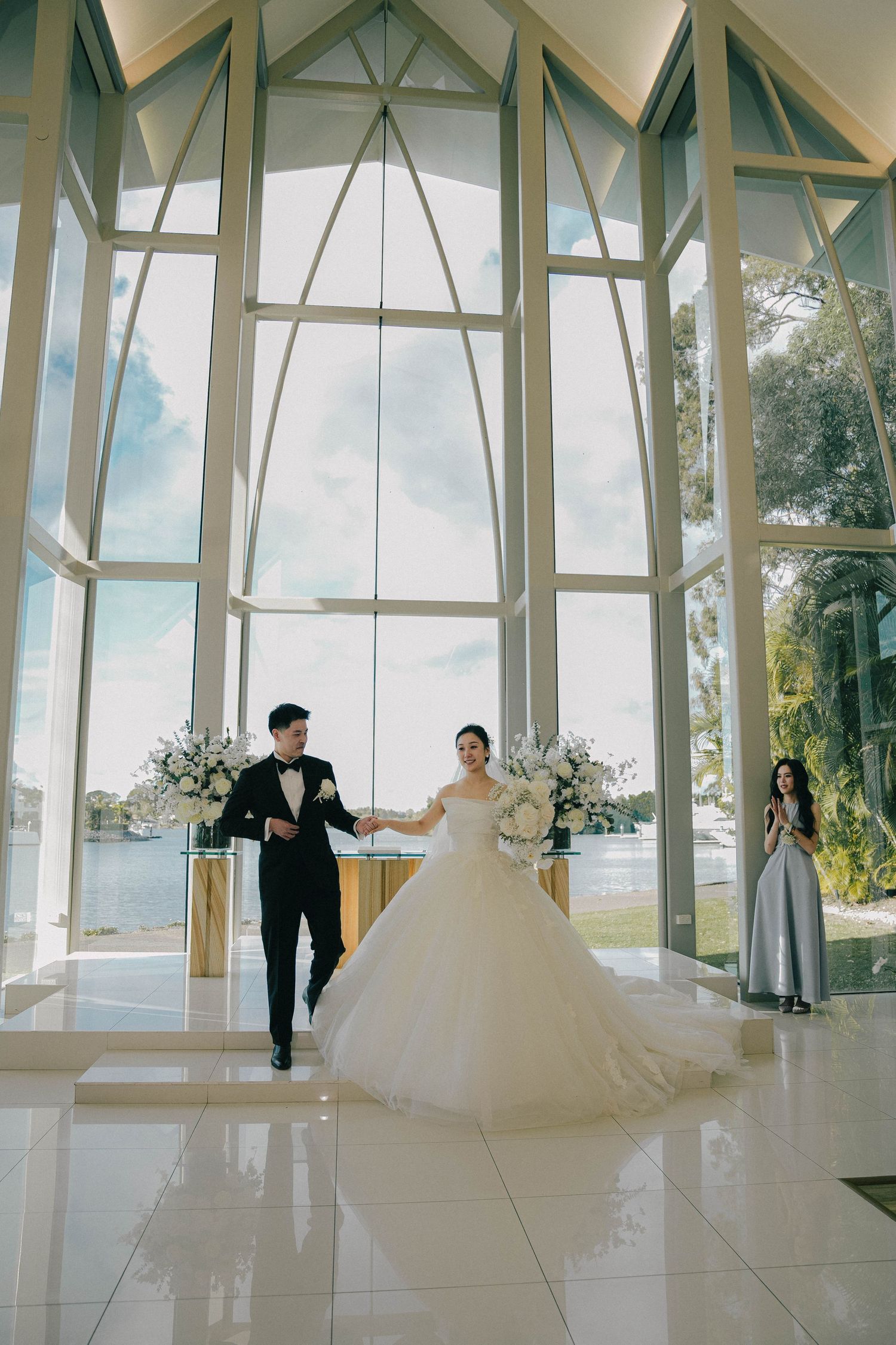 Wedding dresses on display in a modern glass-walled chapel with scenic views of nature outside.