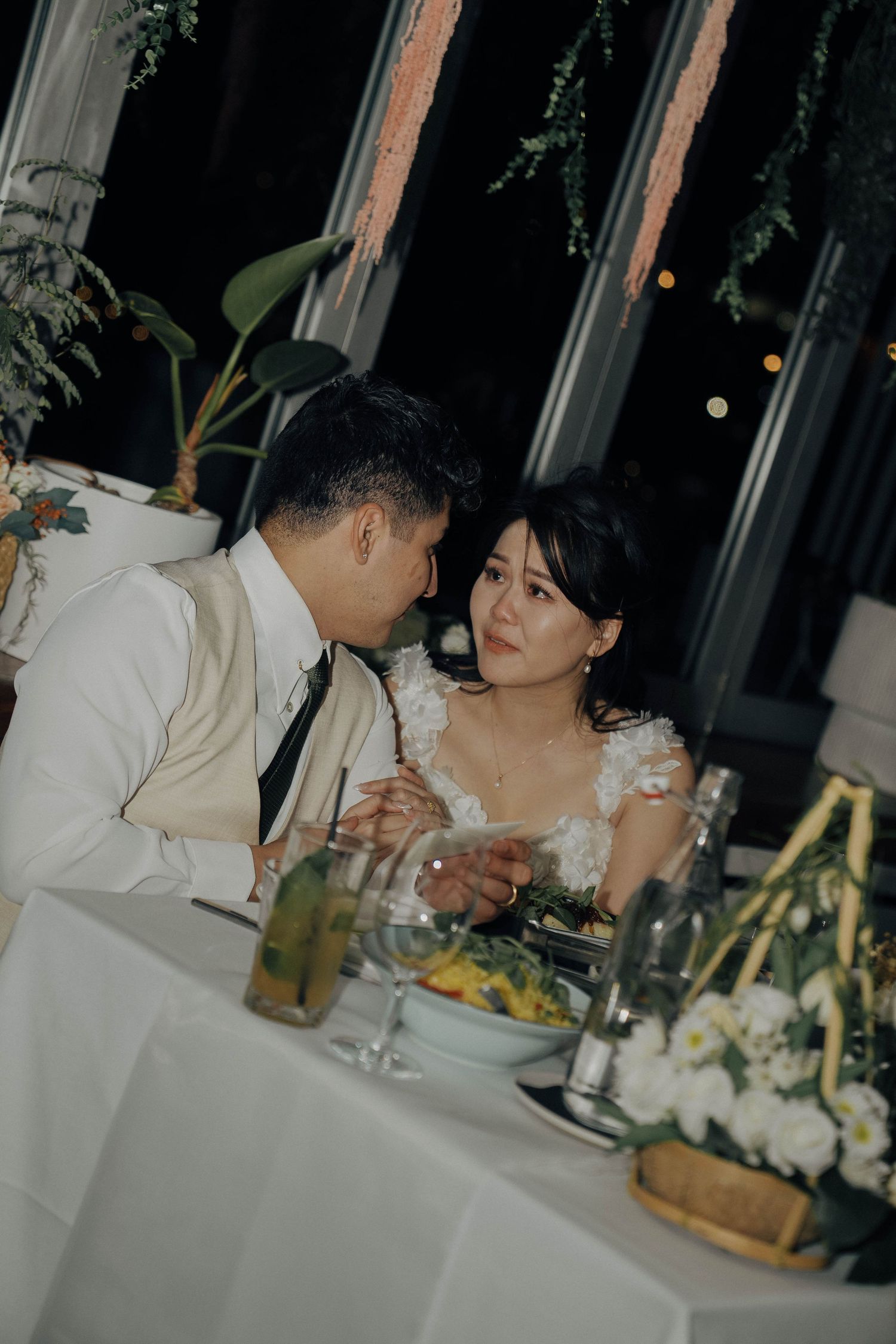 Couple sharing an intimate moment at an elegant dinner table decorated with flowers and candlelight.