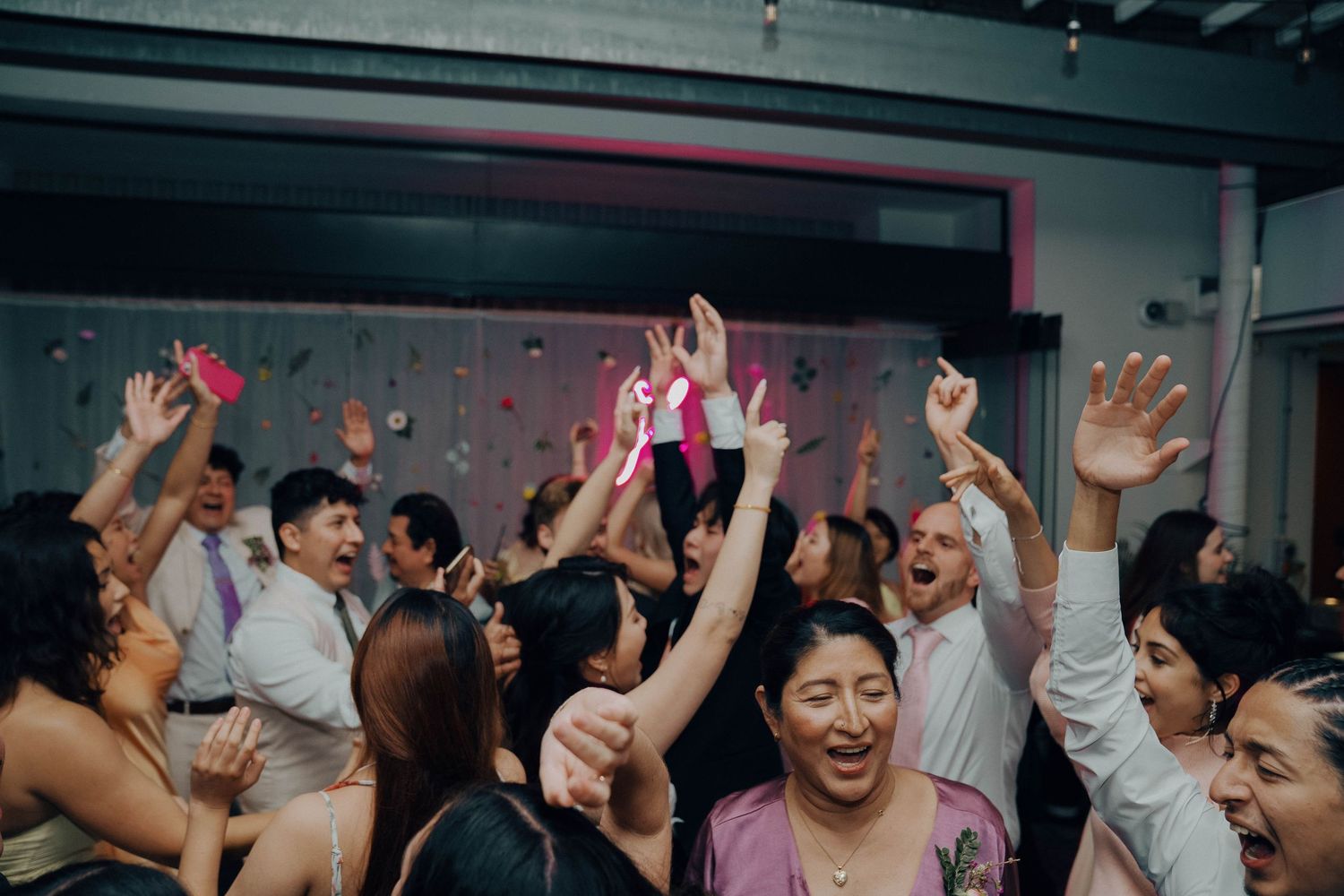 Joyful crowd with raised arms enjoying themselves on a dance floor with colorful lighting.