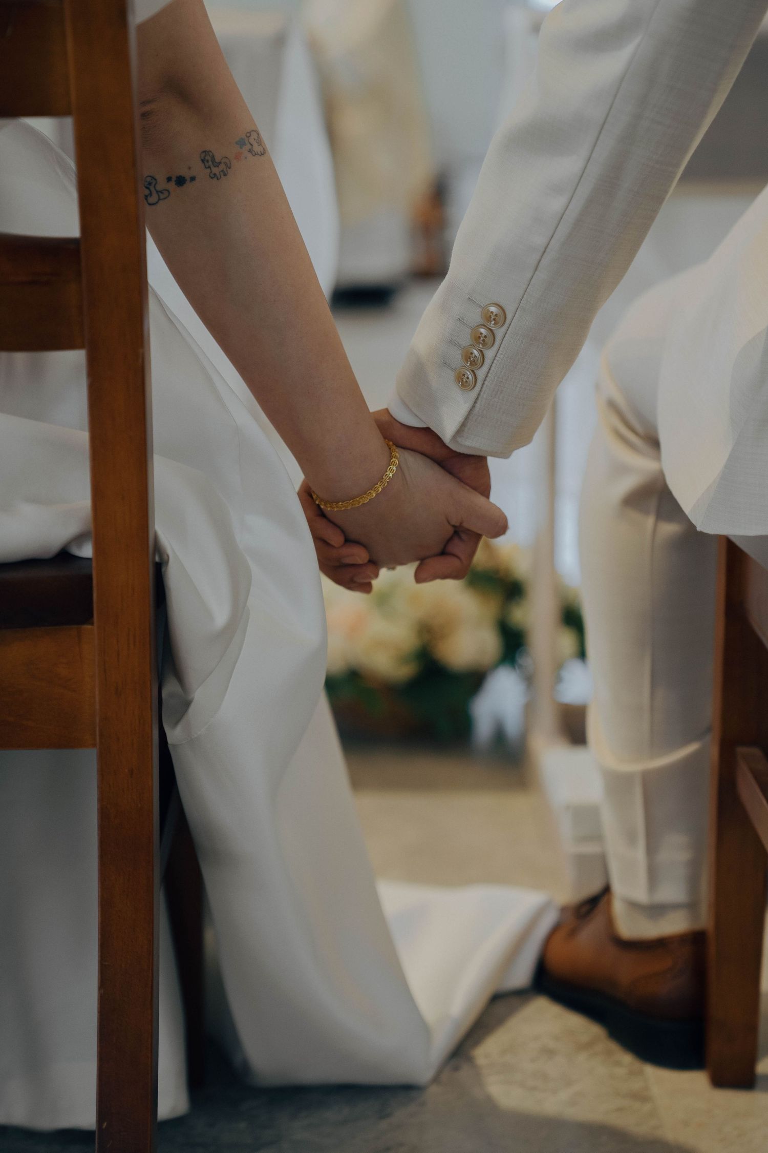 Close-up view of hands adjusting white formal attire while seated in a wooden chair.