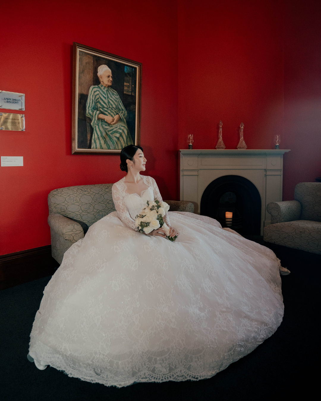 A series of four photos showing a bride in a flowing white lace gown posing on a sofa against a deep red wall.