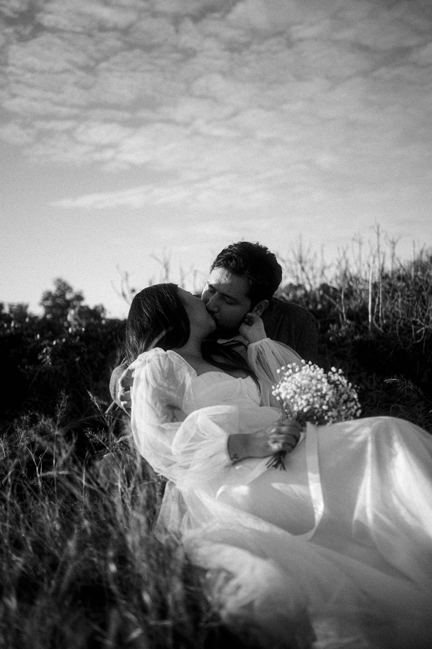 A romantic black and white wedding photo series showing a couple embracing in a field with flowing white dress details.