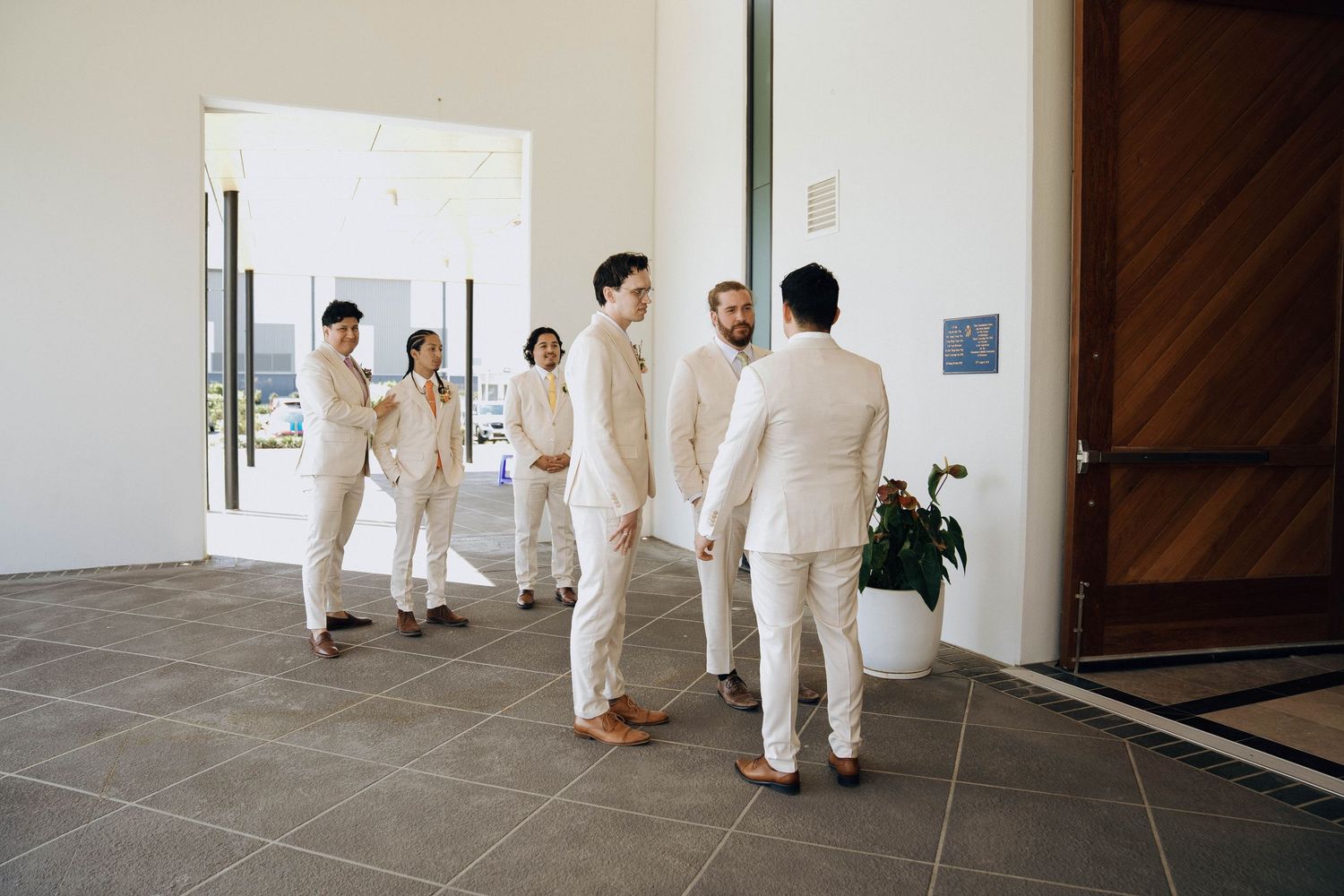 A group of people wearing all white clothing walk down a minimalist hallway with concrete floors.