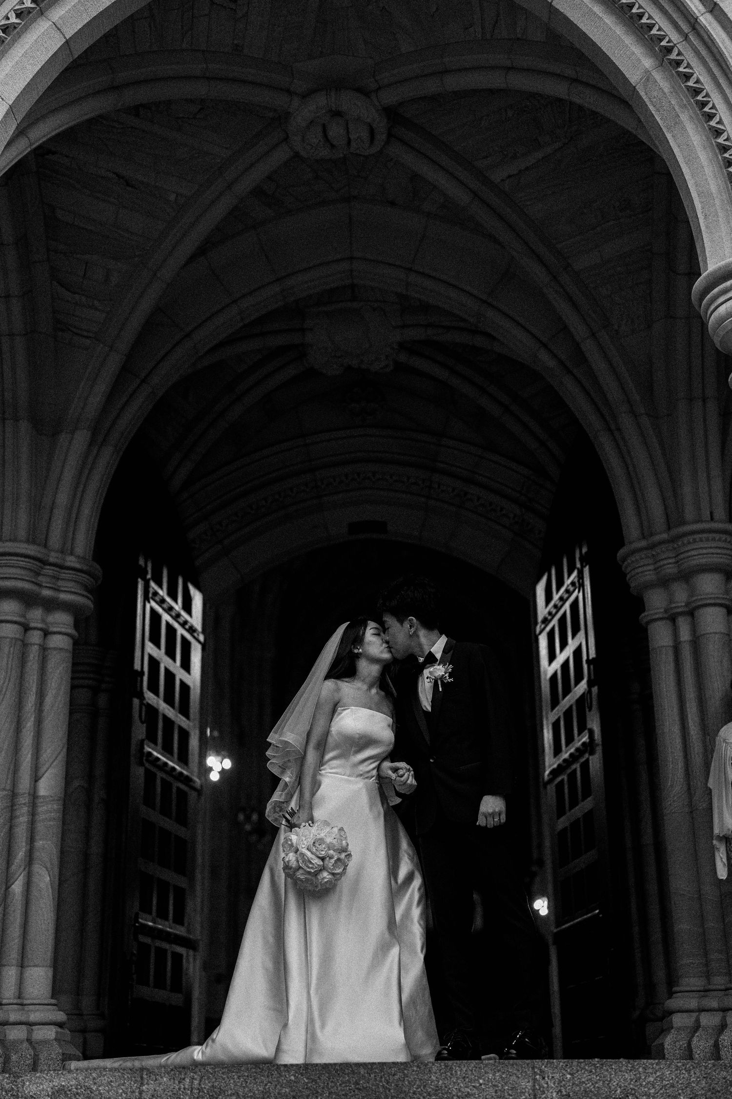 Black and white wedding photograph series showing couple under gothic stone archways at dusk.