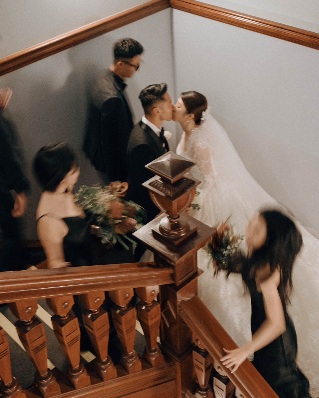 Cinematic capture of a couple in wedding attire ascending a wooden staircase in a dimly lit hallway.