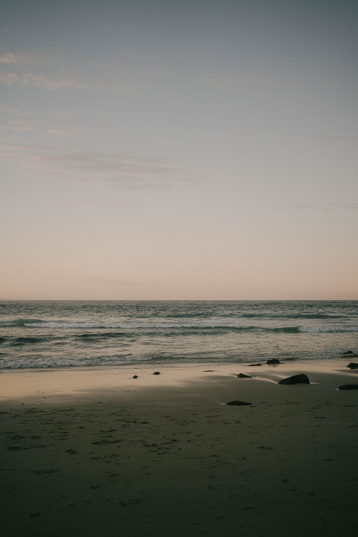A serene panoramic view of a misty beach at dusk with dark rocks scattered along the shoreline and gentle waves rolling in.