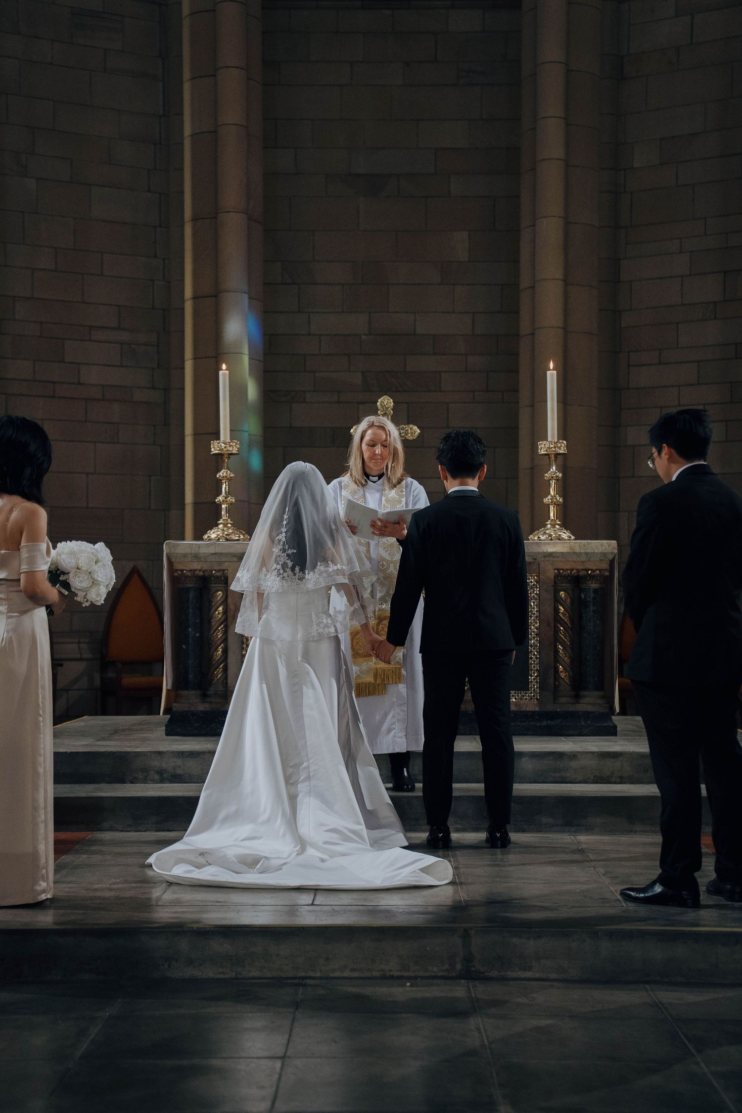 A solemn wedding ceremony moment captured in a dimly lit cathedral with candlelit altar.