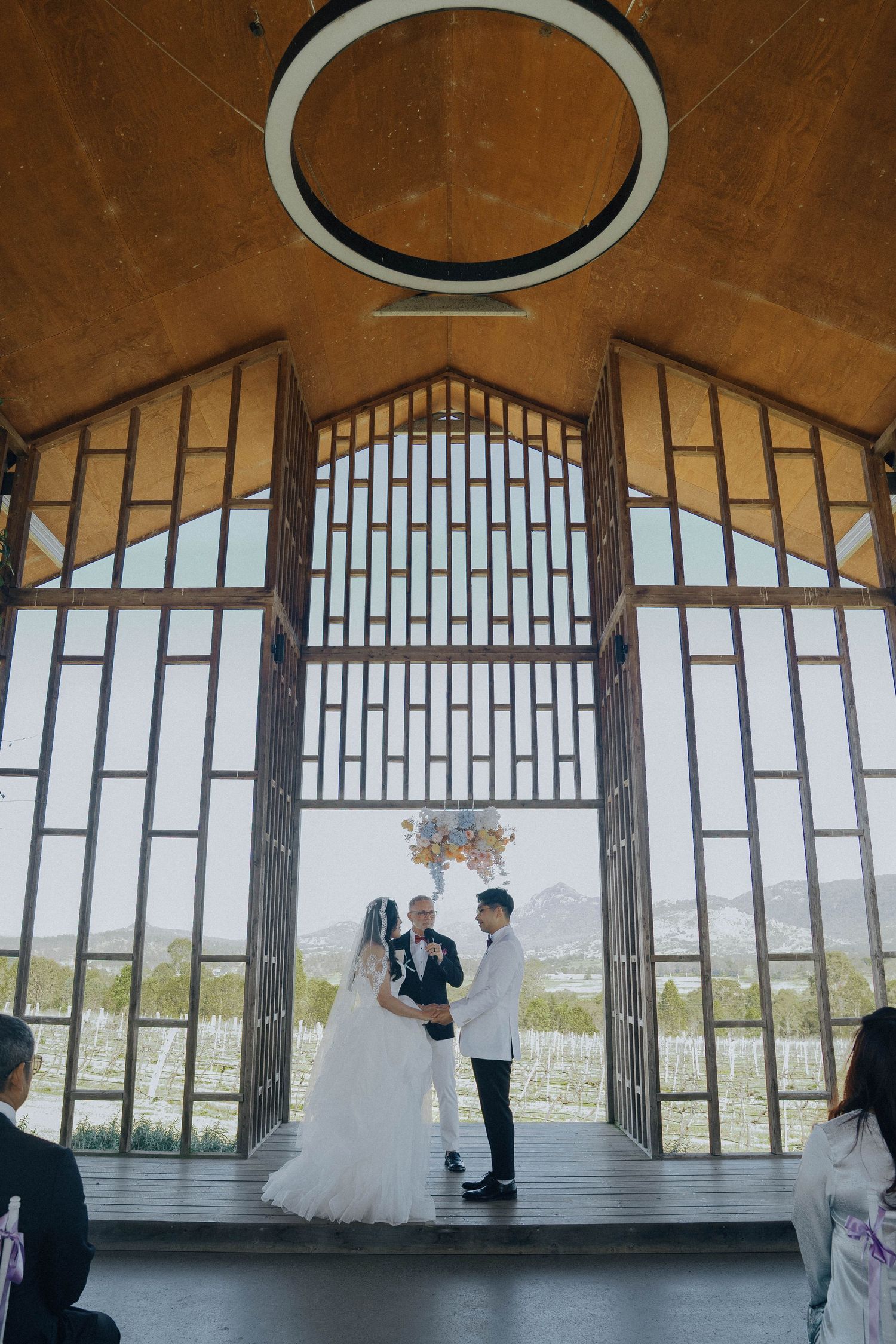 Wedding ceremony taking place in a modern chapel with geometric windows overlooking scenic mountain views.