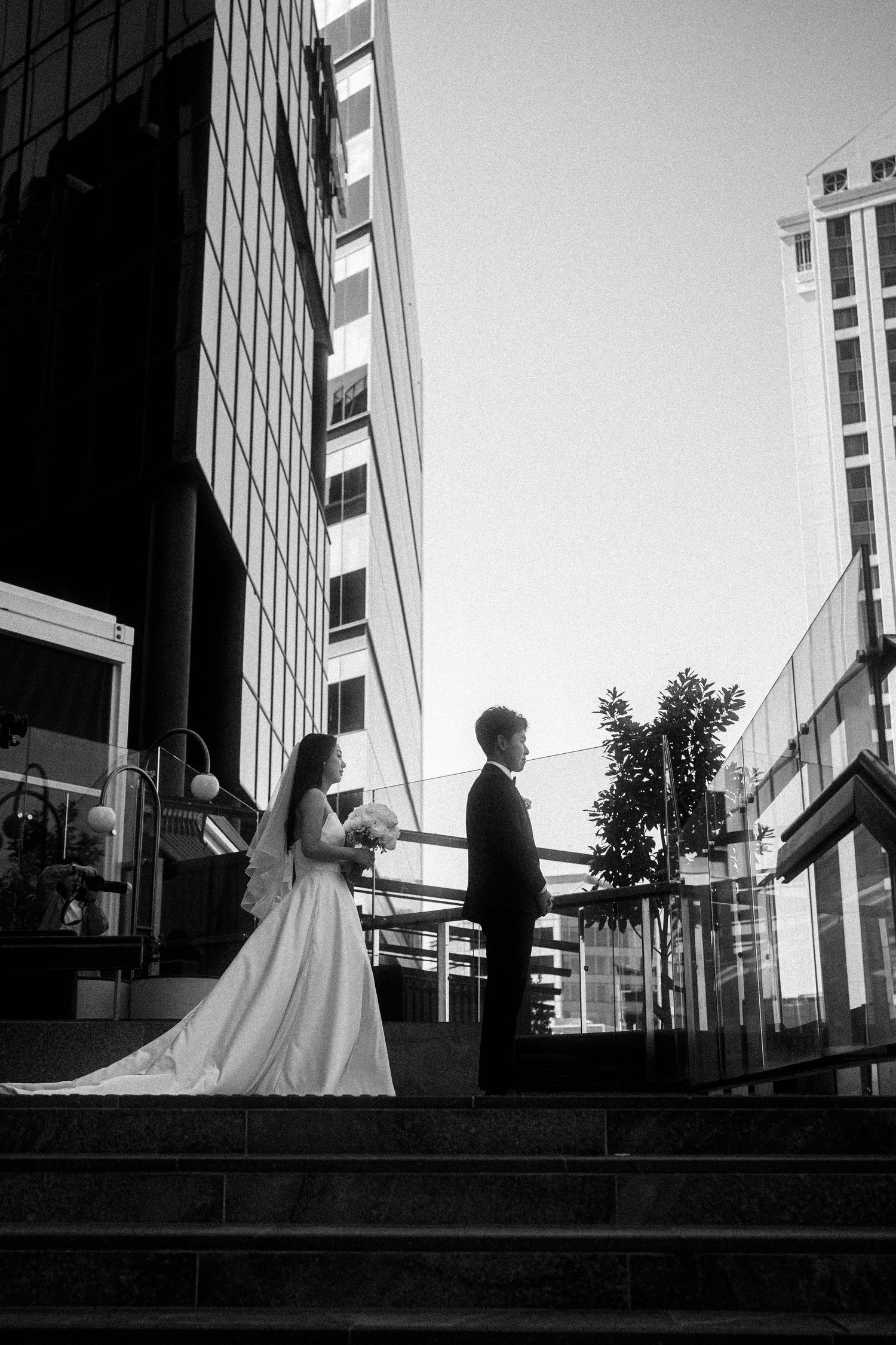 A black and white photo sequence showing a bride and groom walking across a modern urban setting with tall buildings.