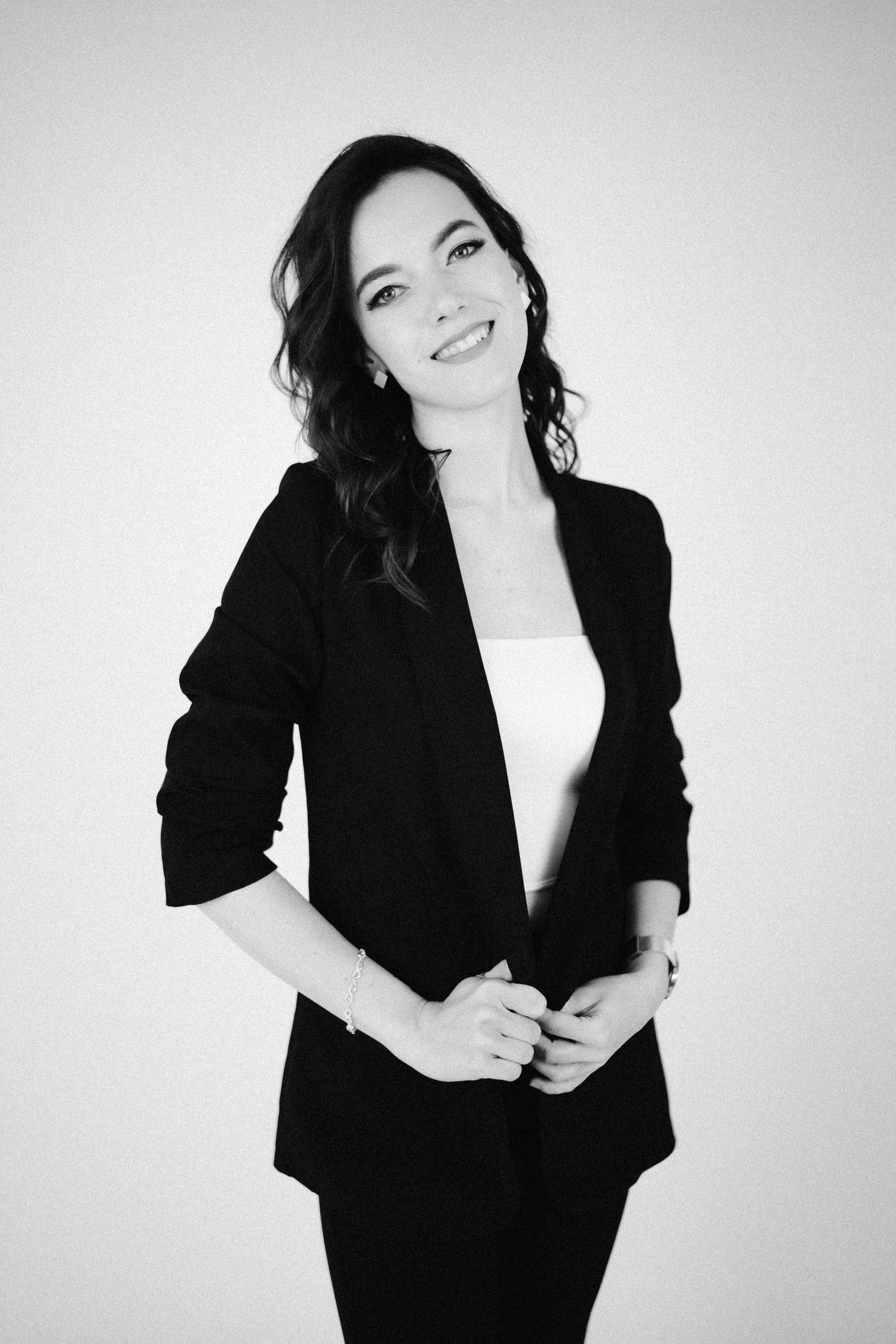 Professional black and white portrait of a person in a black blazer and white top, smiling against a light background.