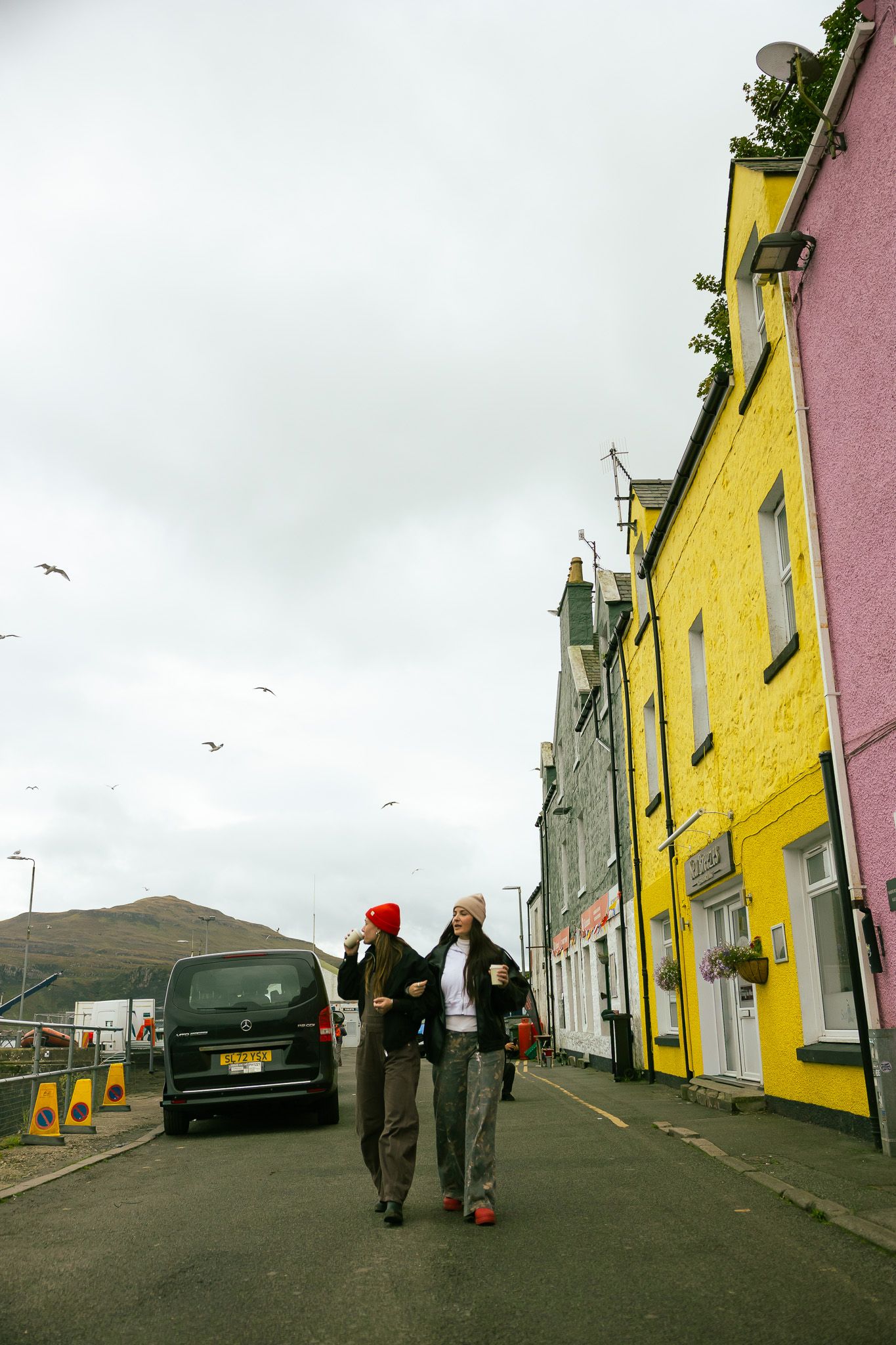 Girls walking by colorful houses at the harbor in Portree, Scotland.