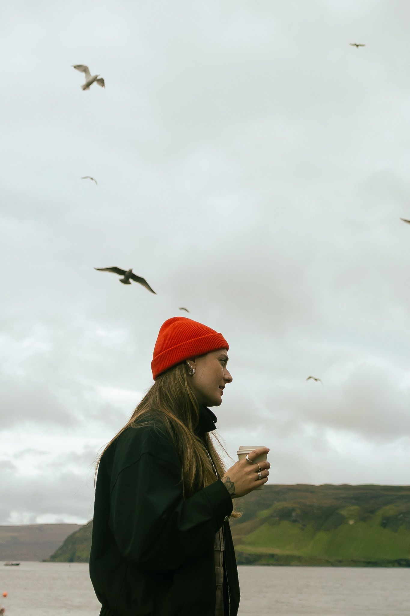 Girl in red beanie enjoying coffee at the harbor in Portree, Scotland.