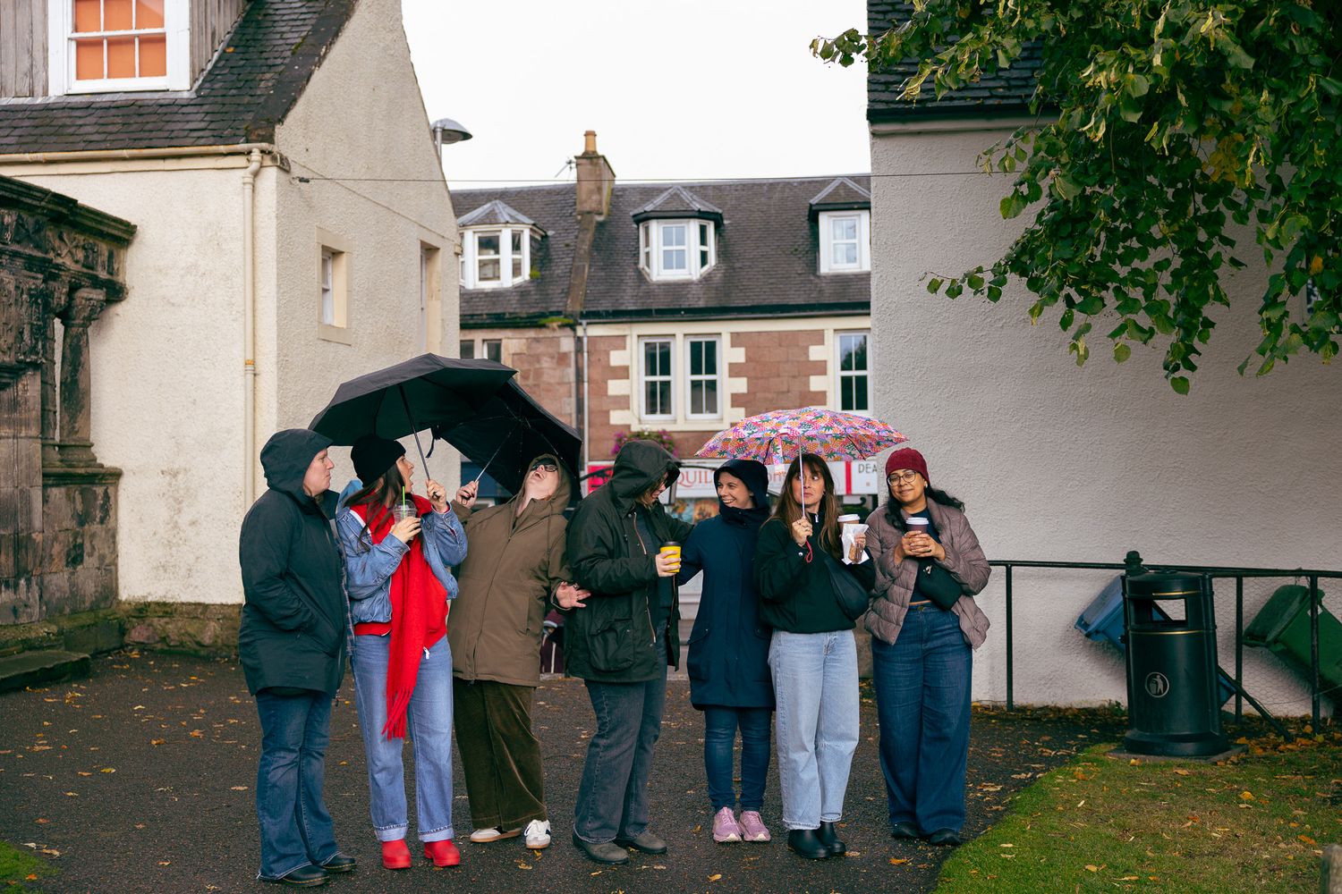 People standing in the rain with umbrellas near a graveyard in Inverness, Scotland.