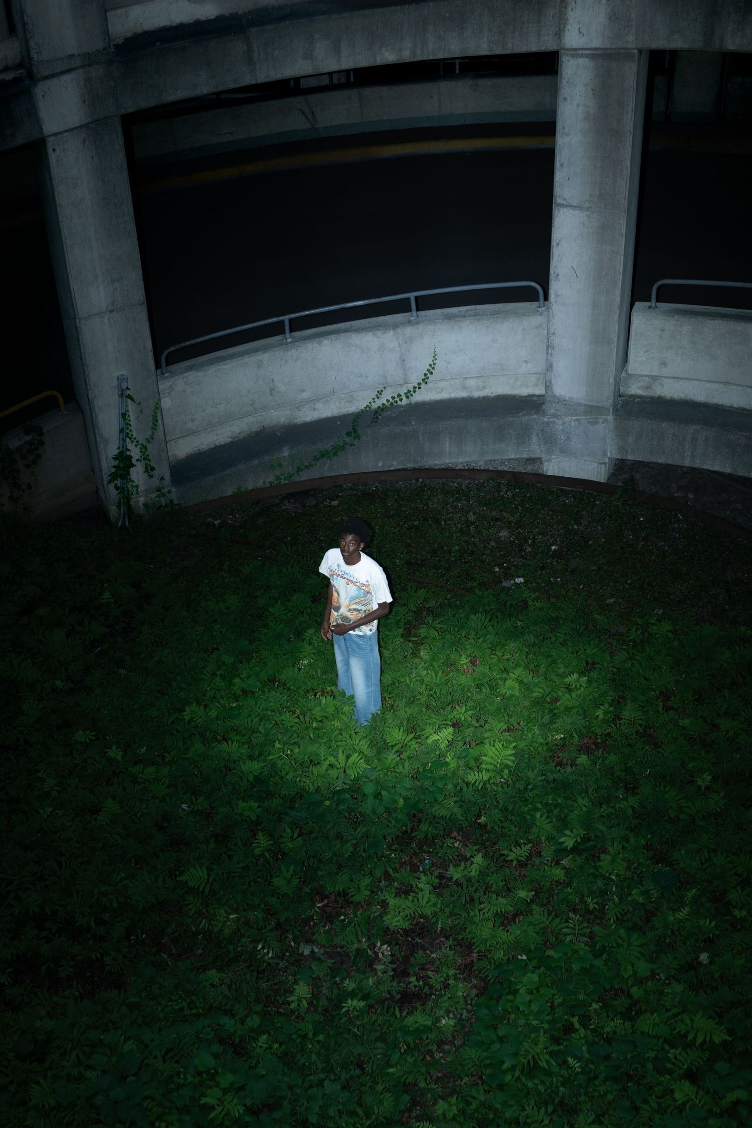 Man in the grass Elmira NY Parking Garage beneath a dark concrete structure in a cinematic portrait
