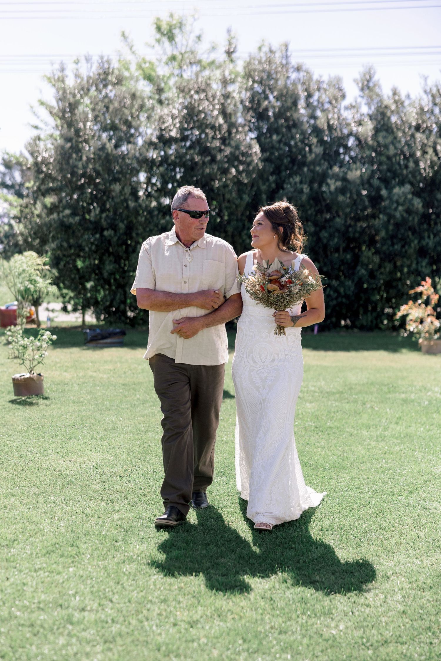 Bride walking arm in arm with her father on a sunny lawn, Hawke's Bay wedding photographer