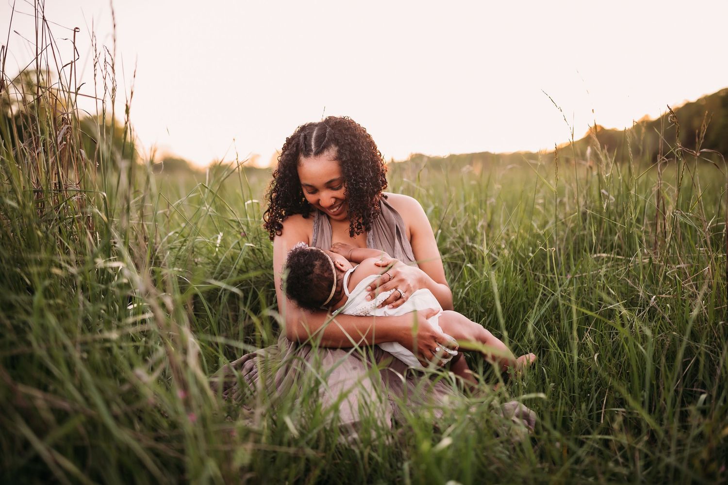 Couple lying together in tall grass during golden hour sunset while taking photos with a camera.