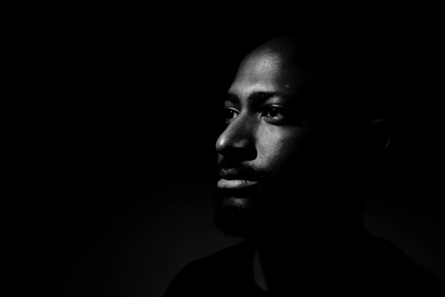 Dramatic black and white portrait of a young man with side lighting against a dark background.