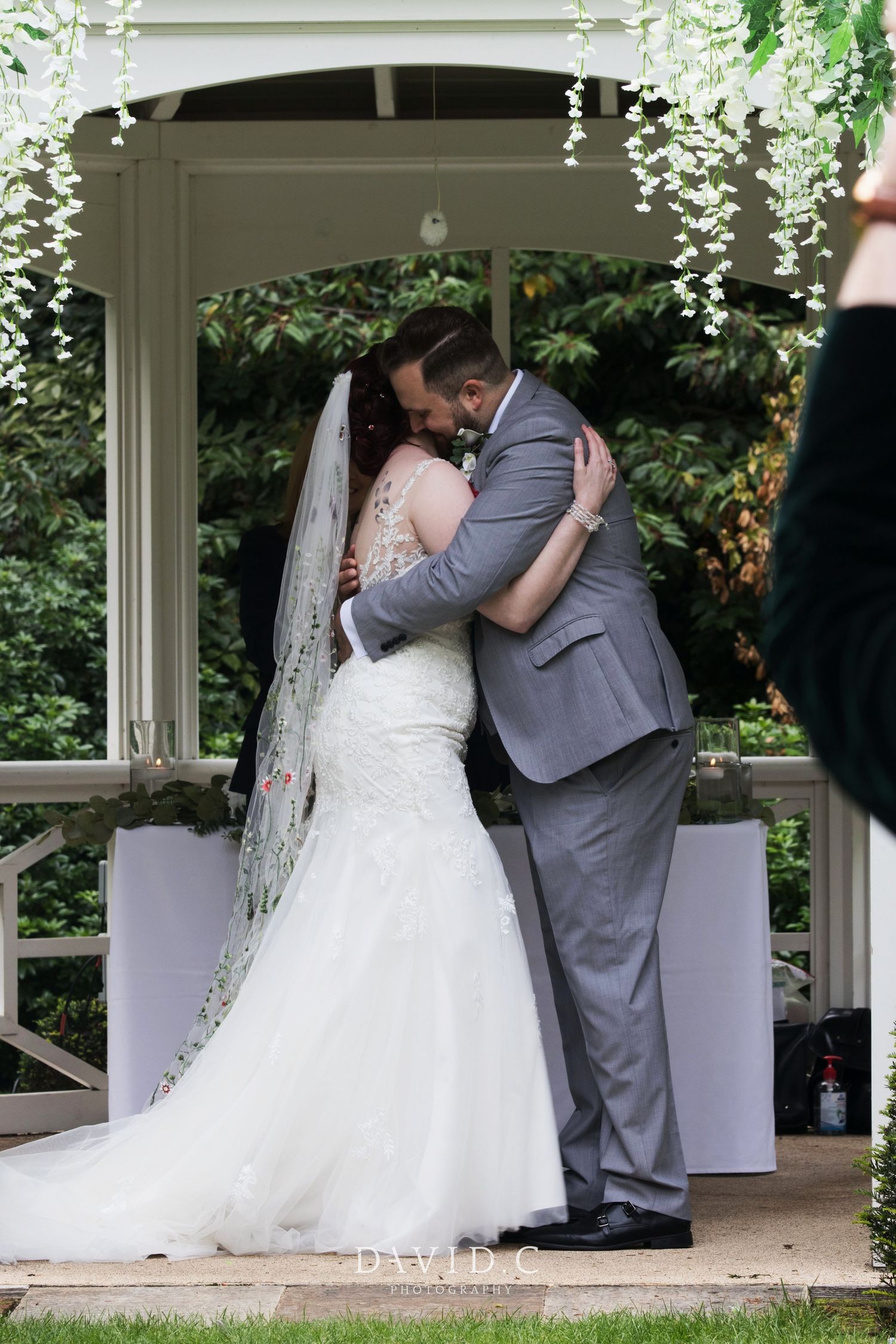 Wedding Photography - Bride and groom sharing their first kiss under a white gazebo decorated with white floral arrangements.