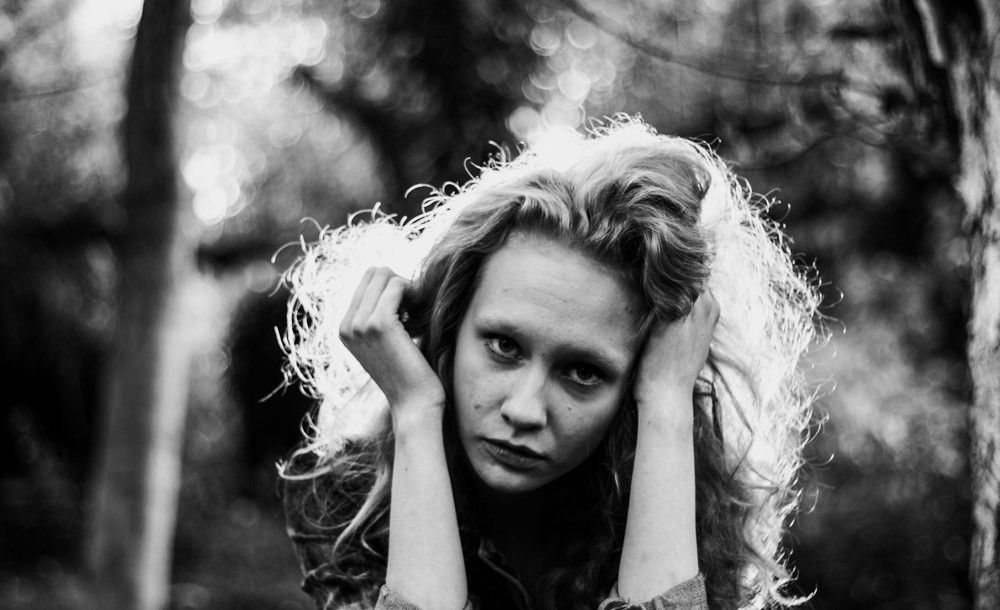 Portrait photography - Black and white portrait of blonde curly-haired woman in forest holding her hair.