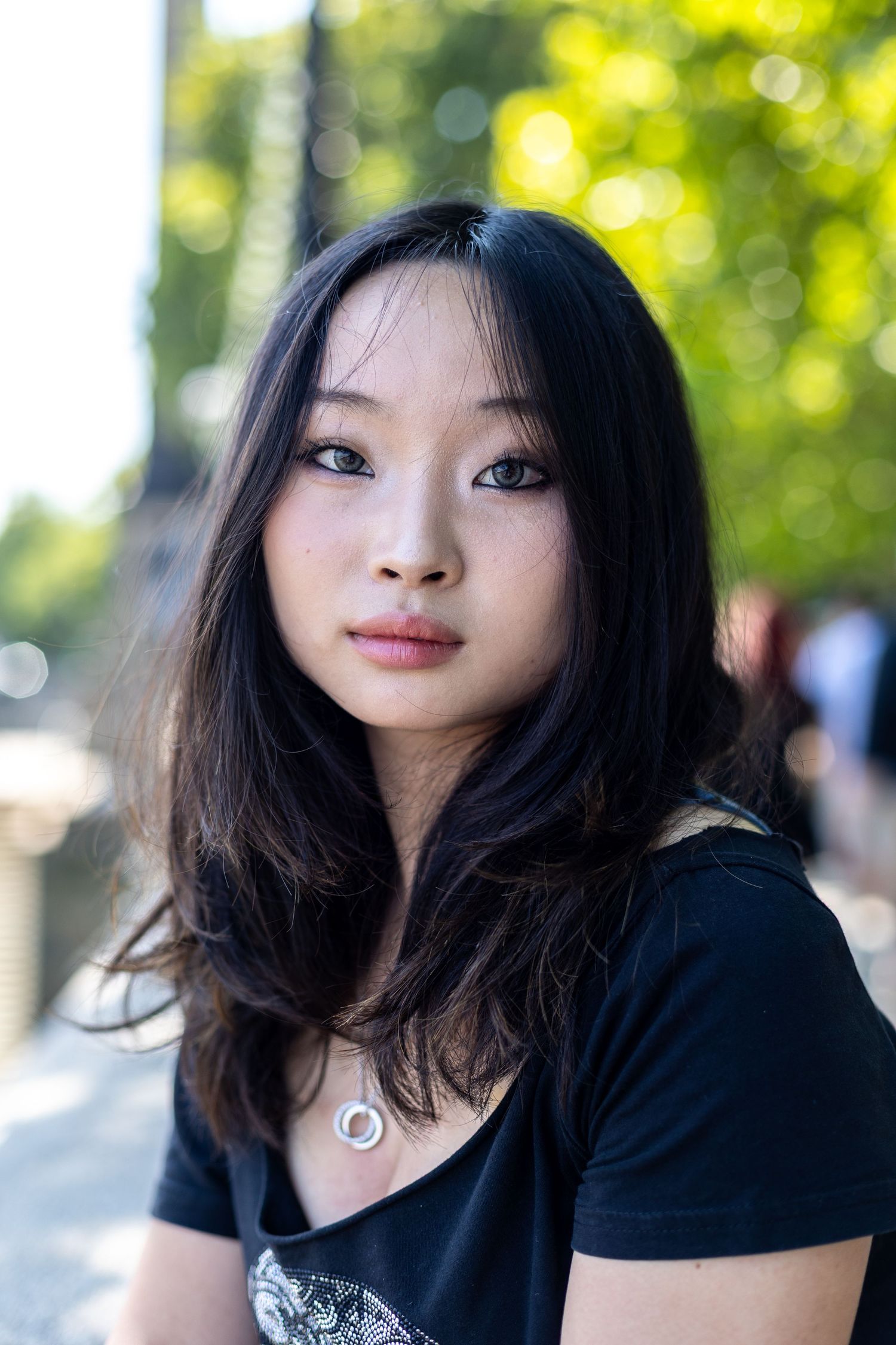 Young Asian woman with dark hair in black t-shirt posing outdoors with bokeh background.