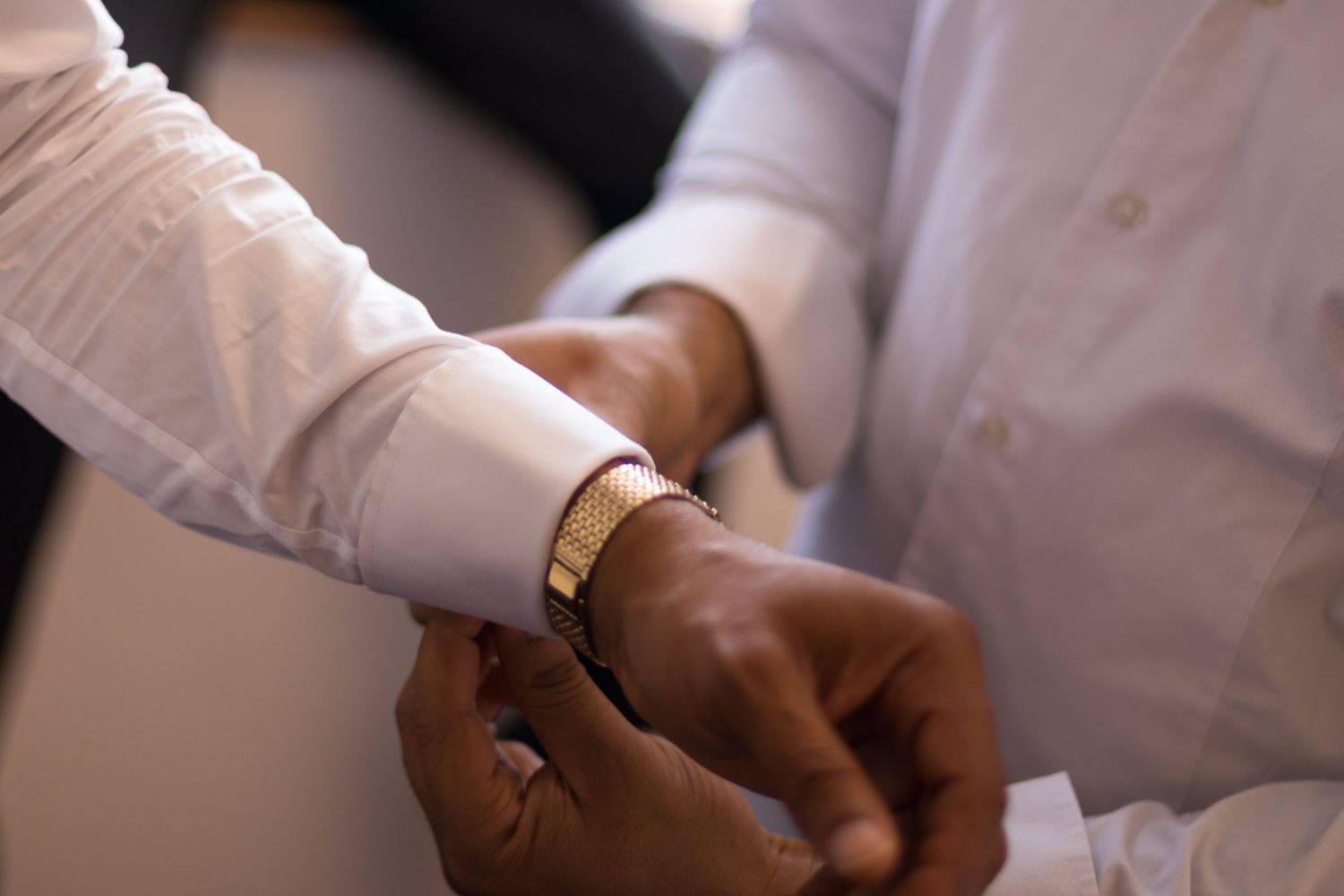 Wedding Photography - Close-up of hands fastening a gold bracelet on a groom's wrist during wedding preparations.
