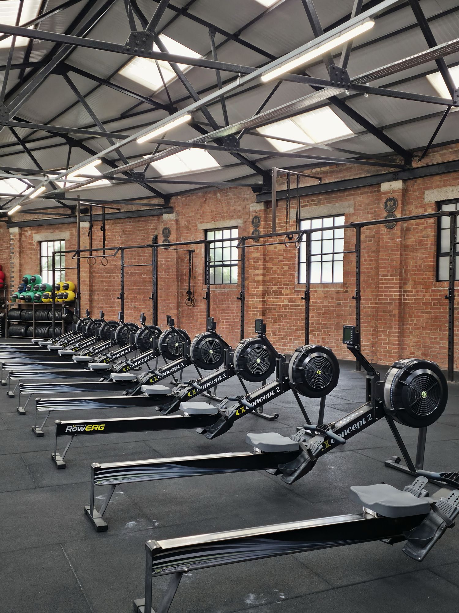 Fitness Photography - Row of Concept2 rowing machines lined up in a spacious brick-walled CrossFit gym.