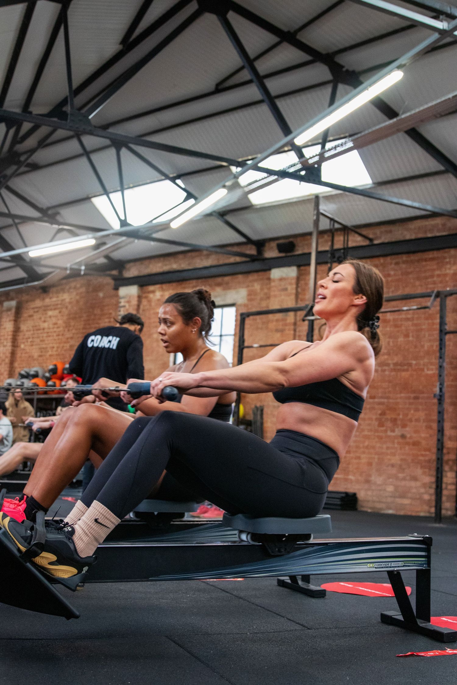 Sports photography -Two women exercising on rowing machines in a modern industrial gym with brick walls.