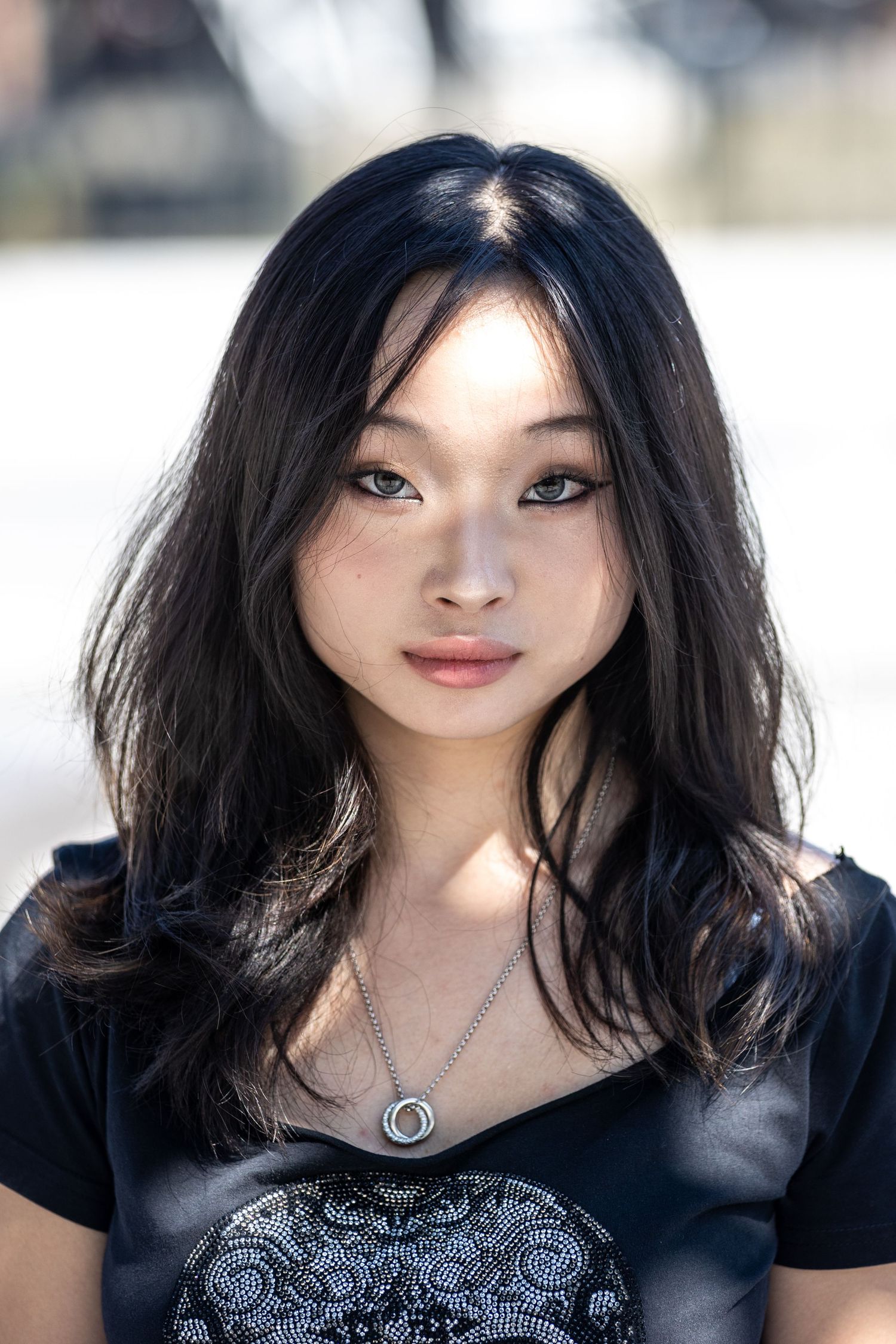 Young Asian woman with long dark hair wearing a black top and silver necklace poses outdoors.