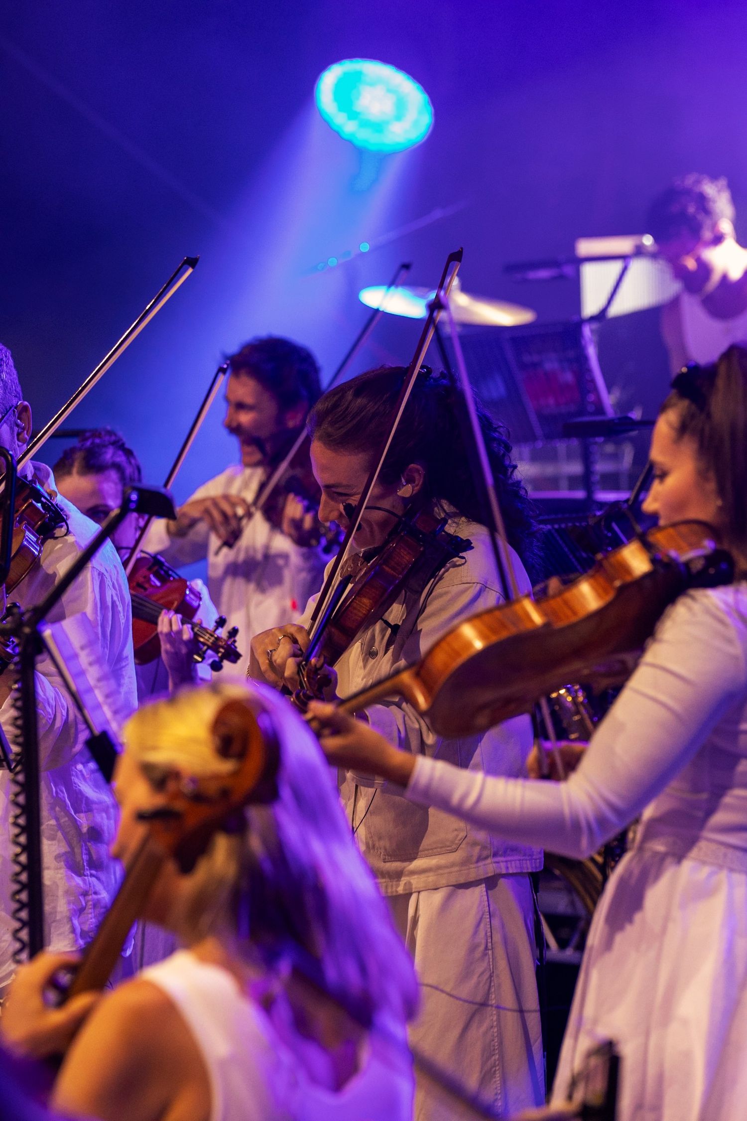 Live Music Event Photography - Group of violinists in white outfits performing on a purple-lit concert stage.