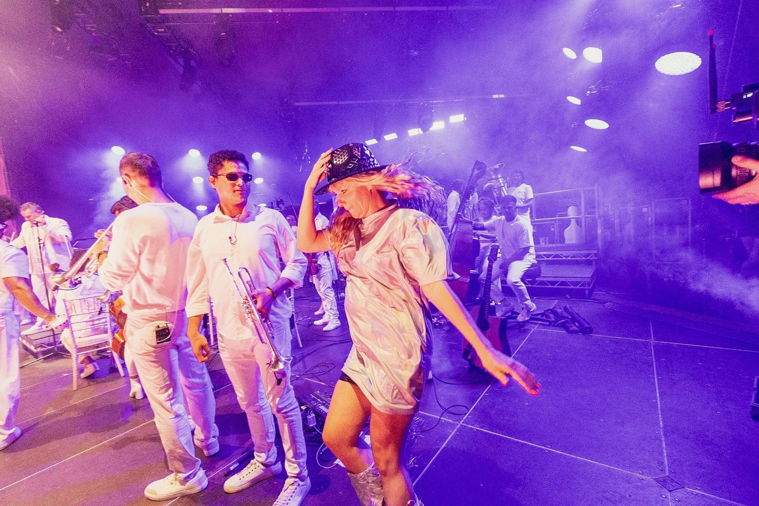 Event Photography - People dancing on stage in white outfits under purple and blue stage lighting at a live music event.
