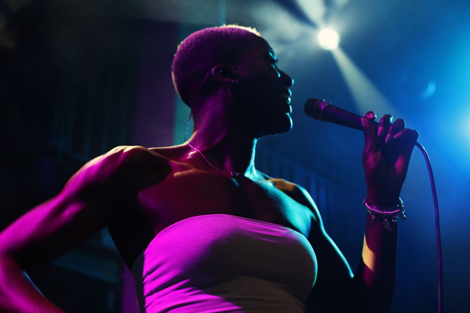 Bald singer performing with a microphone under dramatic blue and pink stage lighting at a live concert.