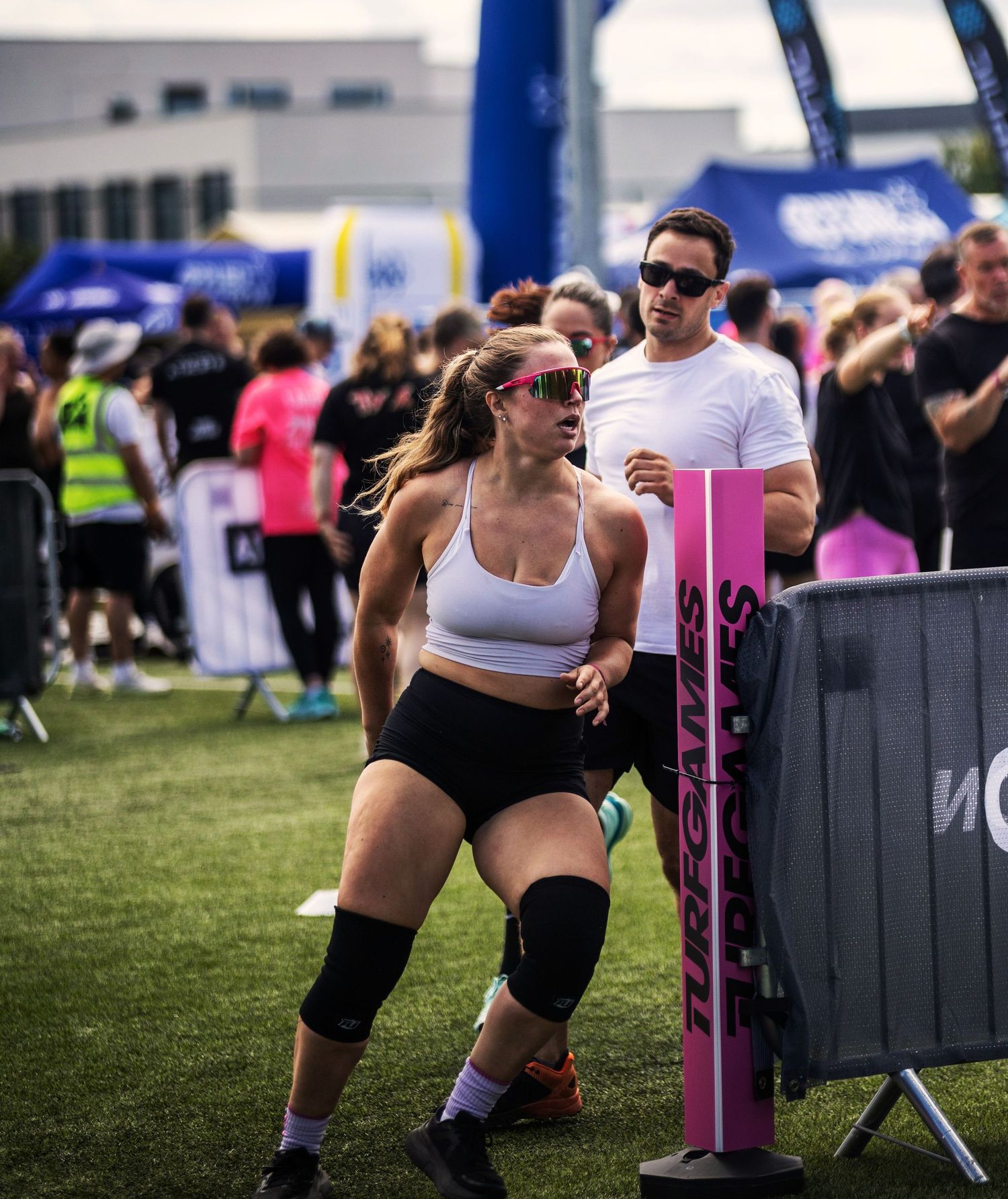 Athletic woman in white sports bra and knee brace competing at an outdoor fitness event.