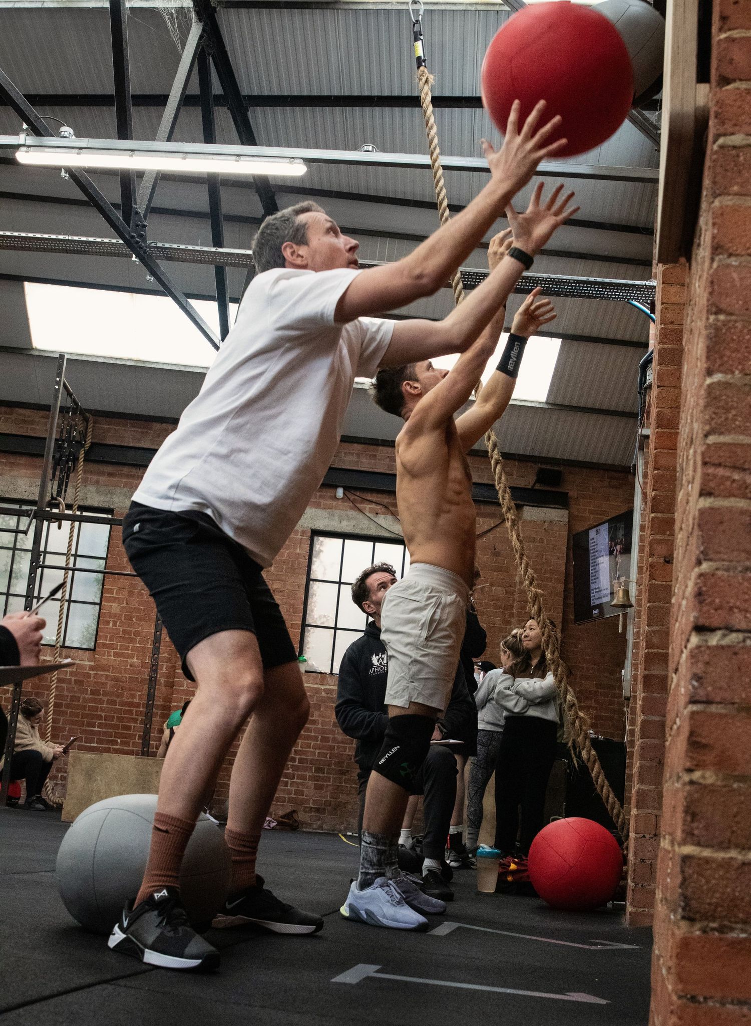 Fitness Photography - Two men throwing a red medicine ball against a wall in an indoor CrossFit gym.