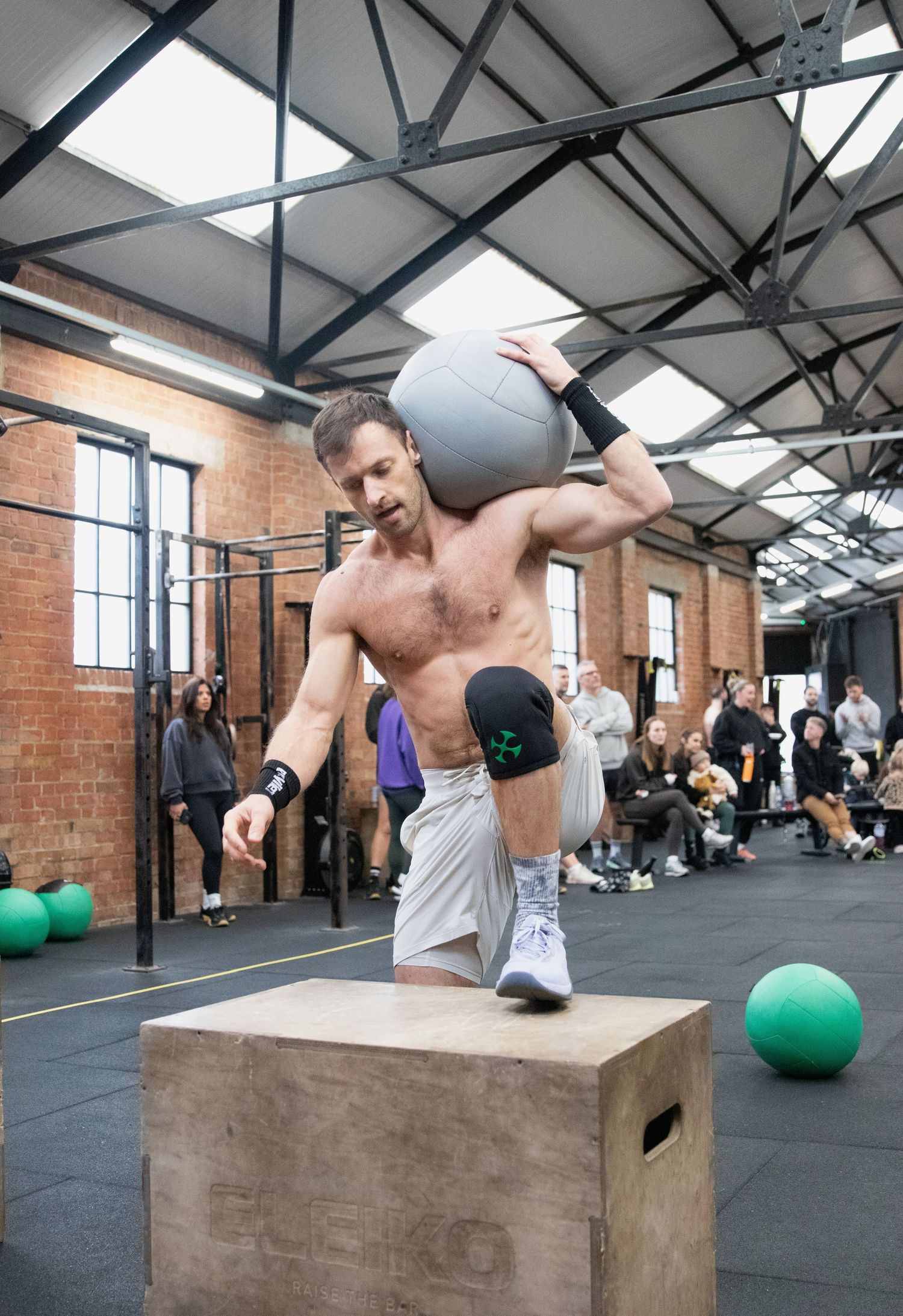 Fitness Photography - Shirtless male athlete stepping onto a wooden box holding a medicine ball overhead.